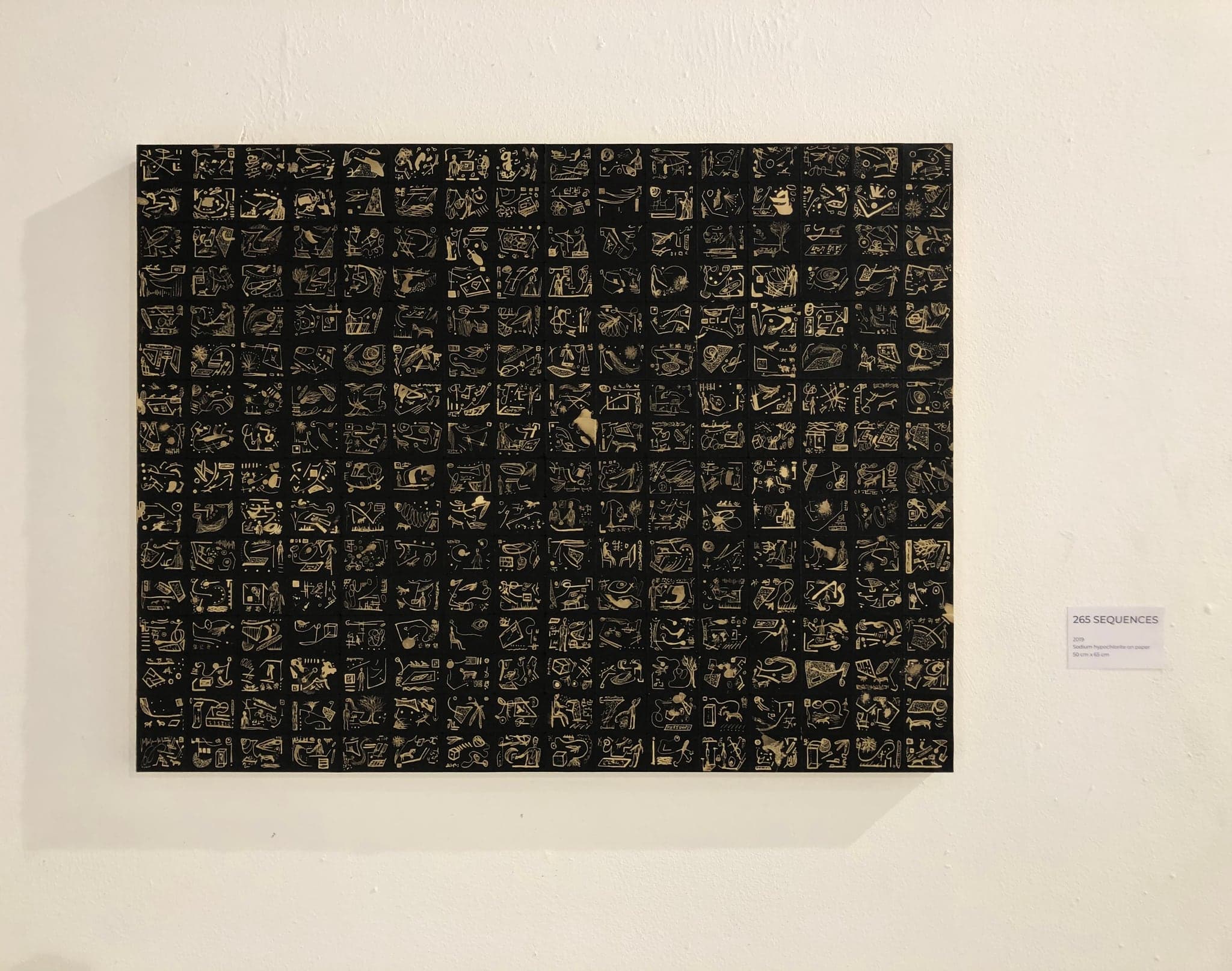 The sheet framed under glass and hung on a white gallery wall, with a small printed label to its right