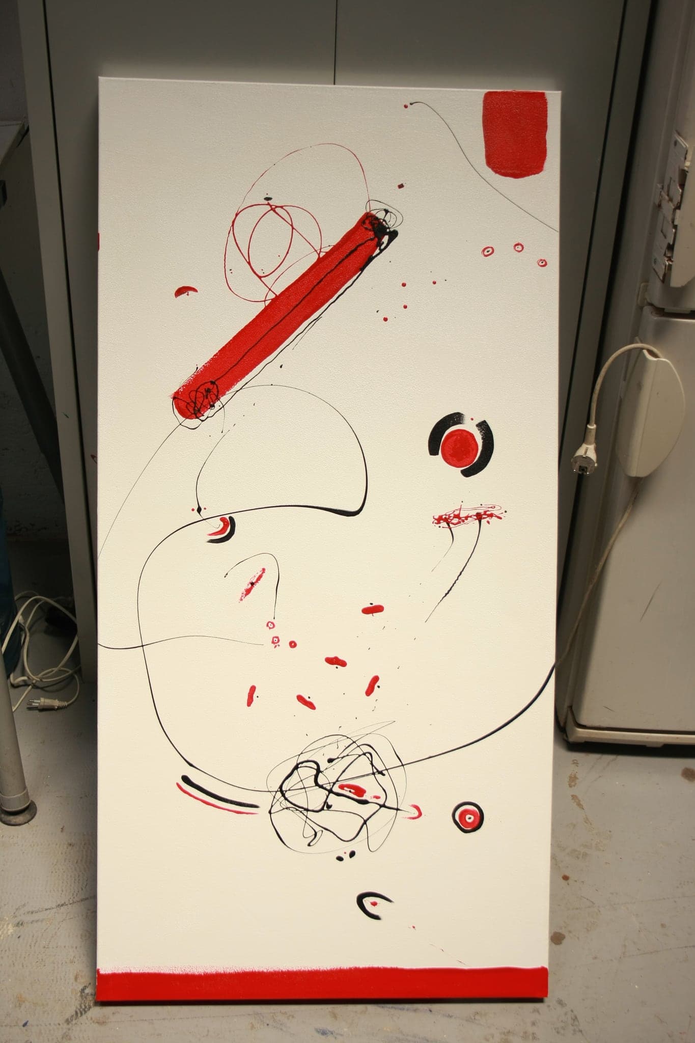 A tall canvas standing in a room, a red bar near the top and scribbled knots below it