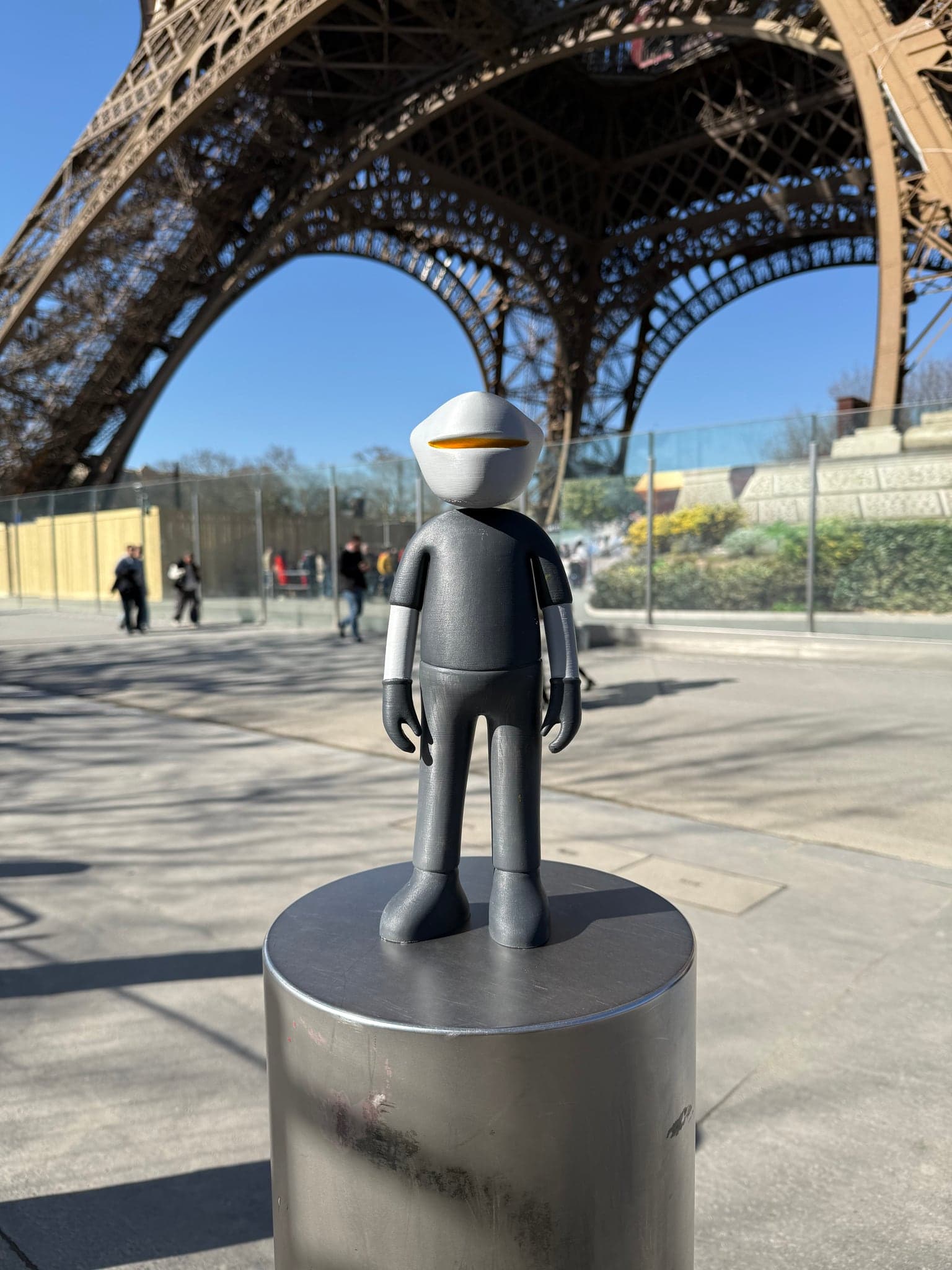 Mr. B alone on a metal bollard under the Eiffel Tower, seen wider