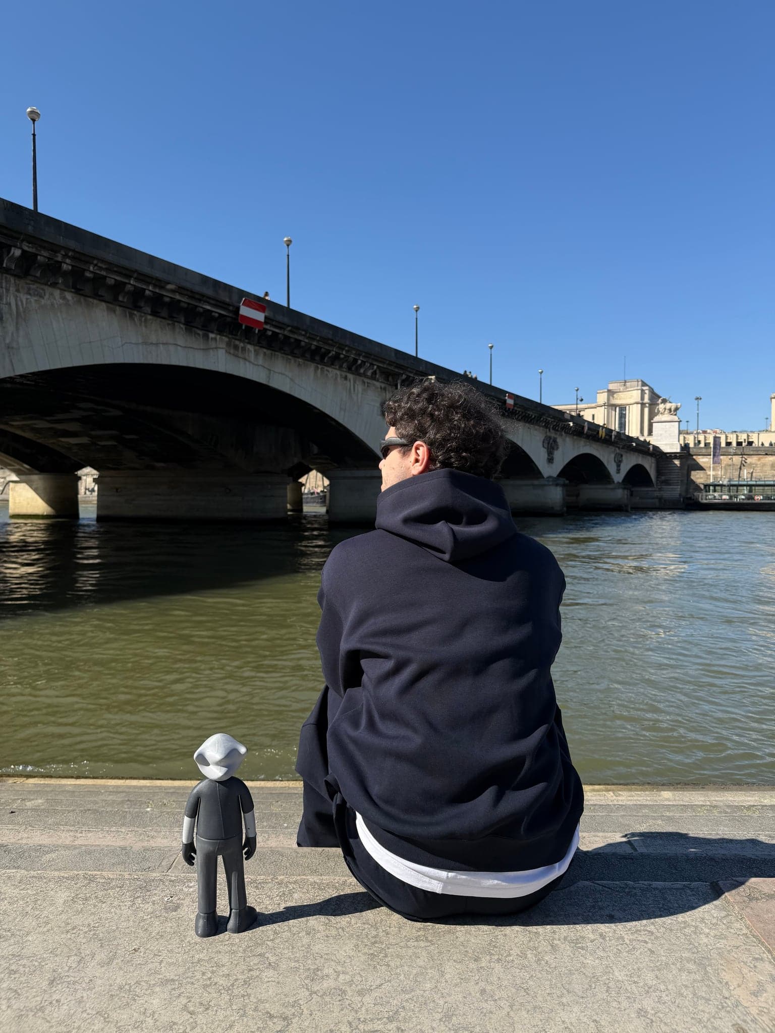 Mr. B standing on the quay beside a seated figure seen from behind, a bridge crossing the Seine ahead