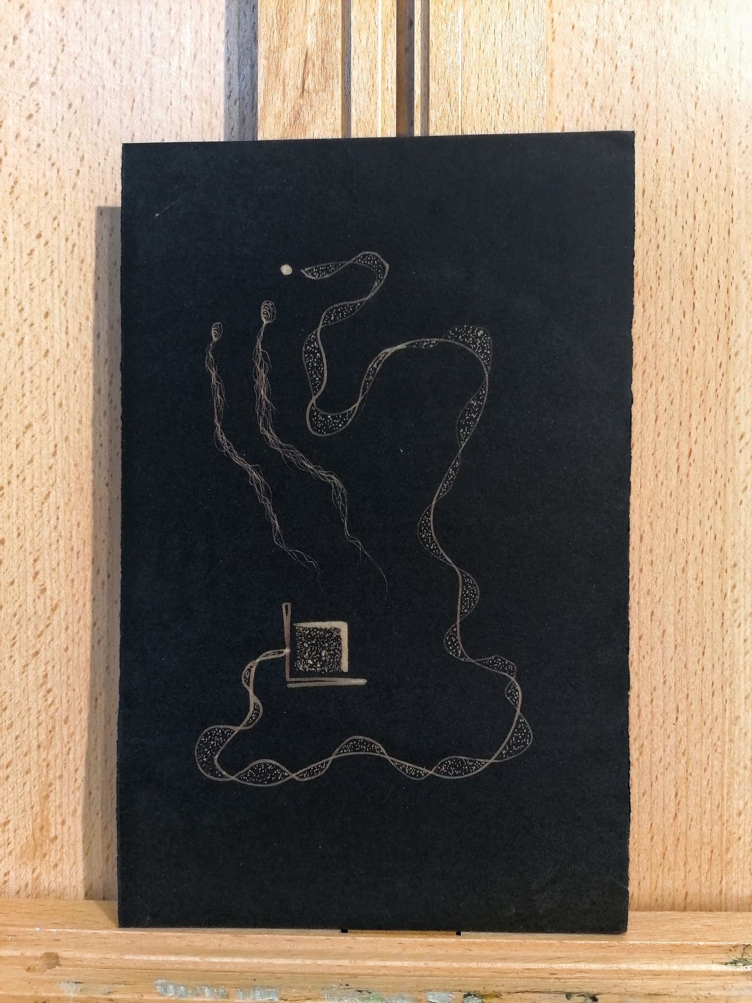 A black sheet drawn in a continuous pale looping line that encloses a small square frame near the bottom
