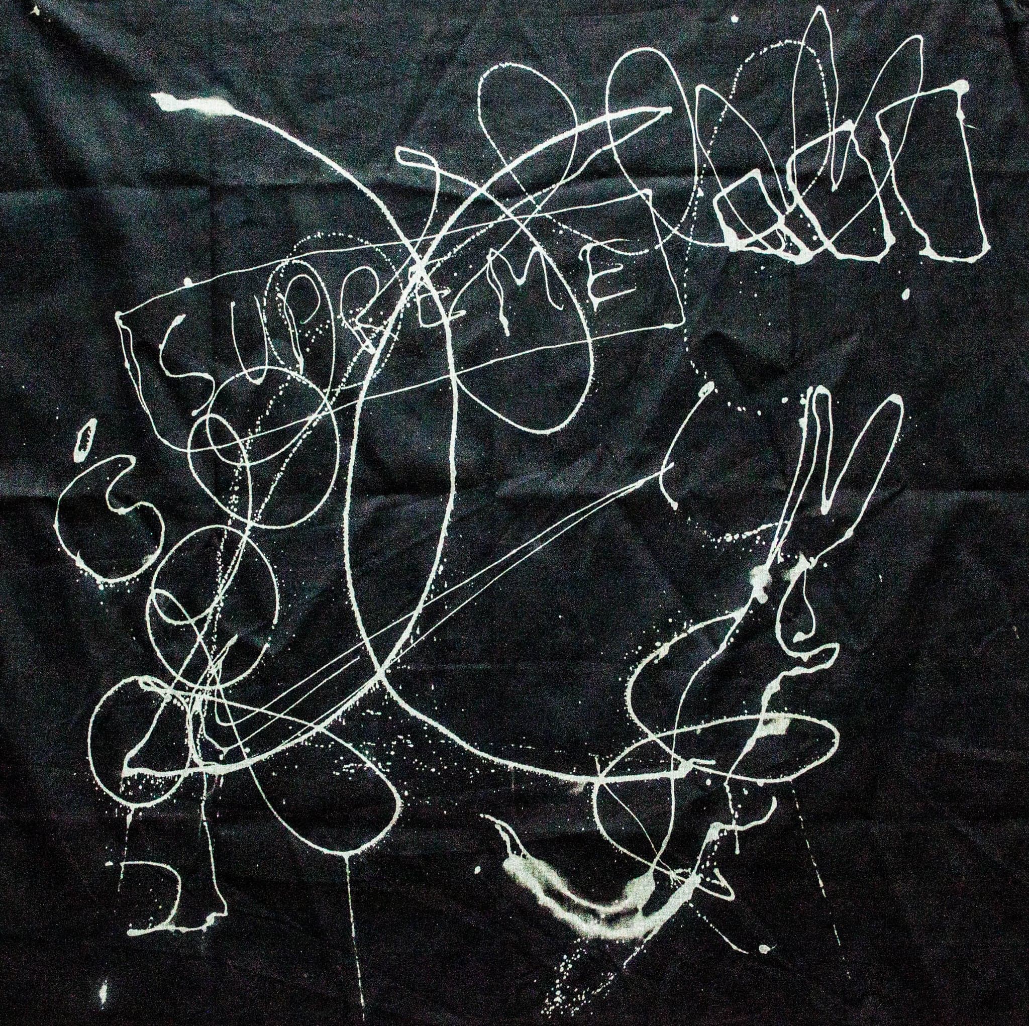 A black sheet carrying one large white looping scrawl with letters caught inside it.