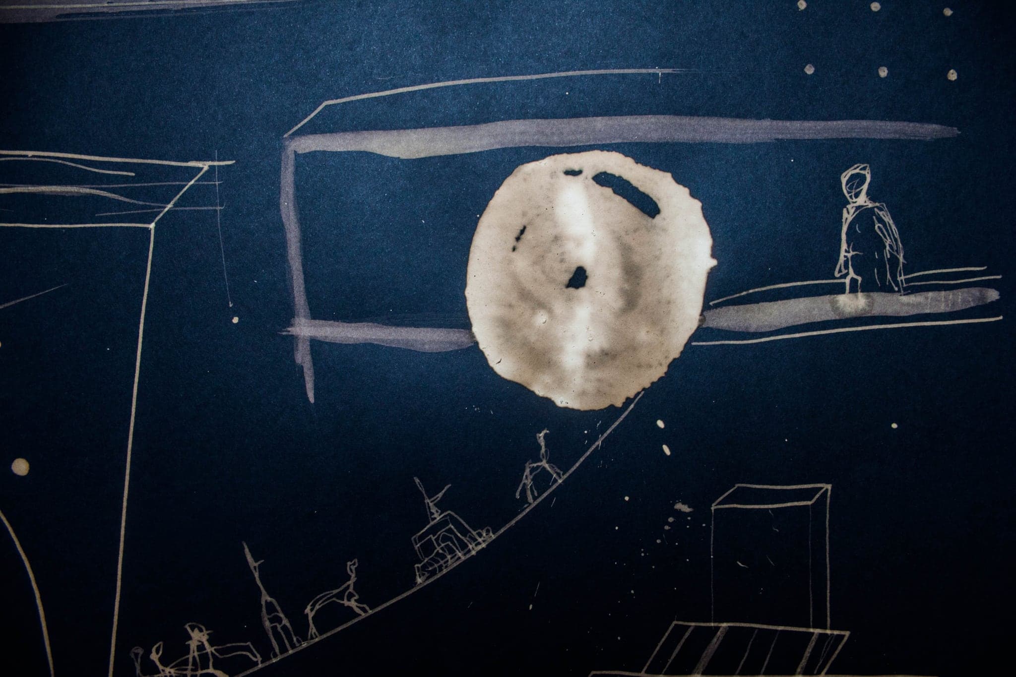A blue sheet holding a pale disc like a moon, a small standing figure and a drawn structure below it.