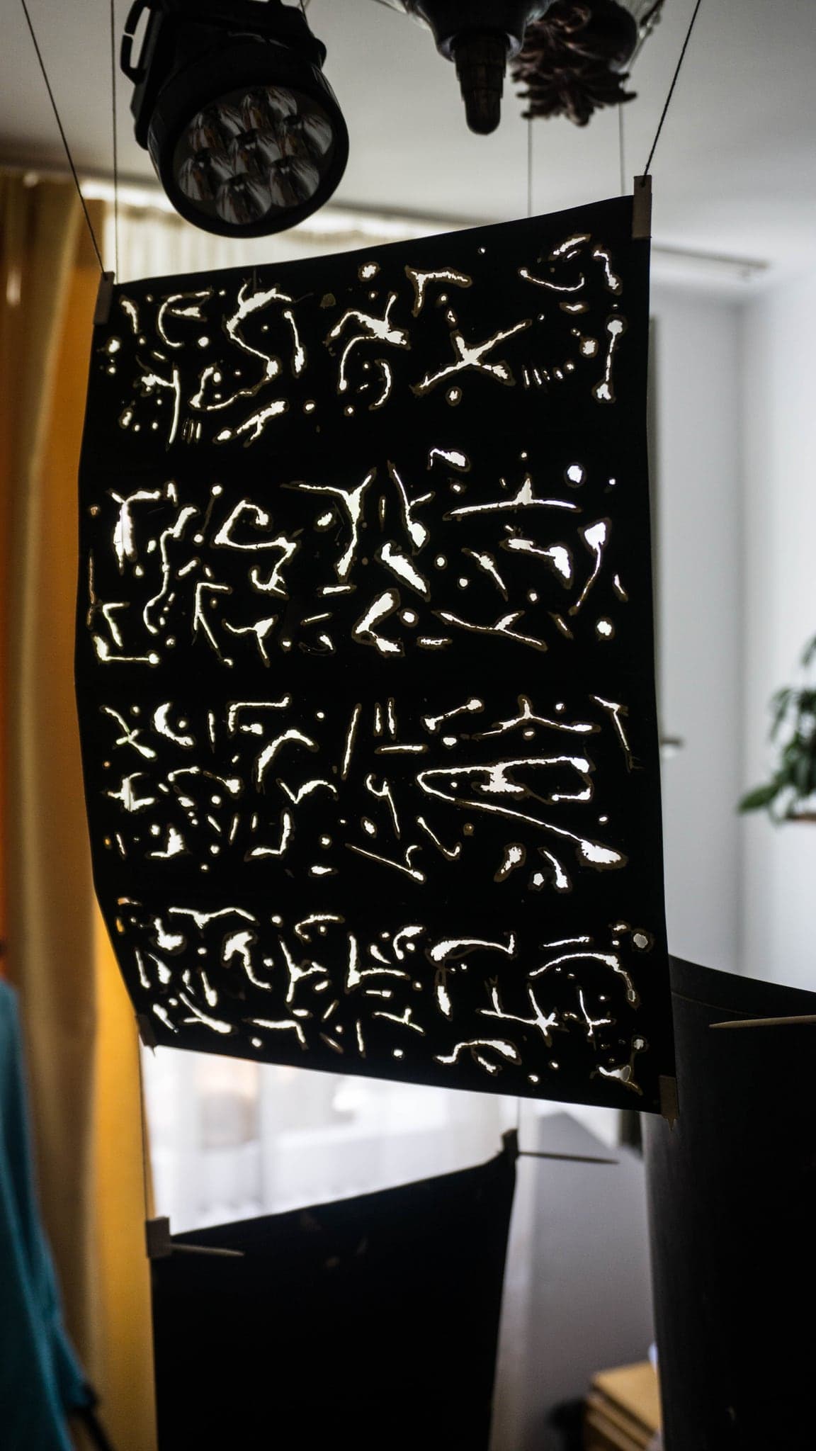 The same sheet seen wider, hanging free between a spotlight above and a yellow curtain behind it.