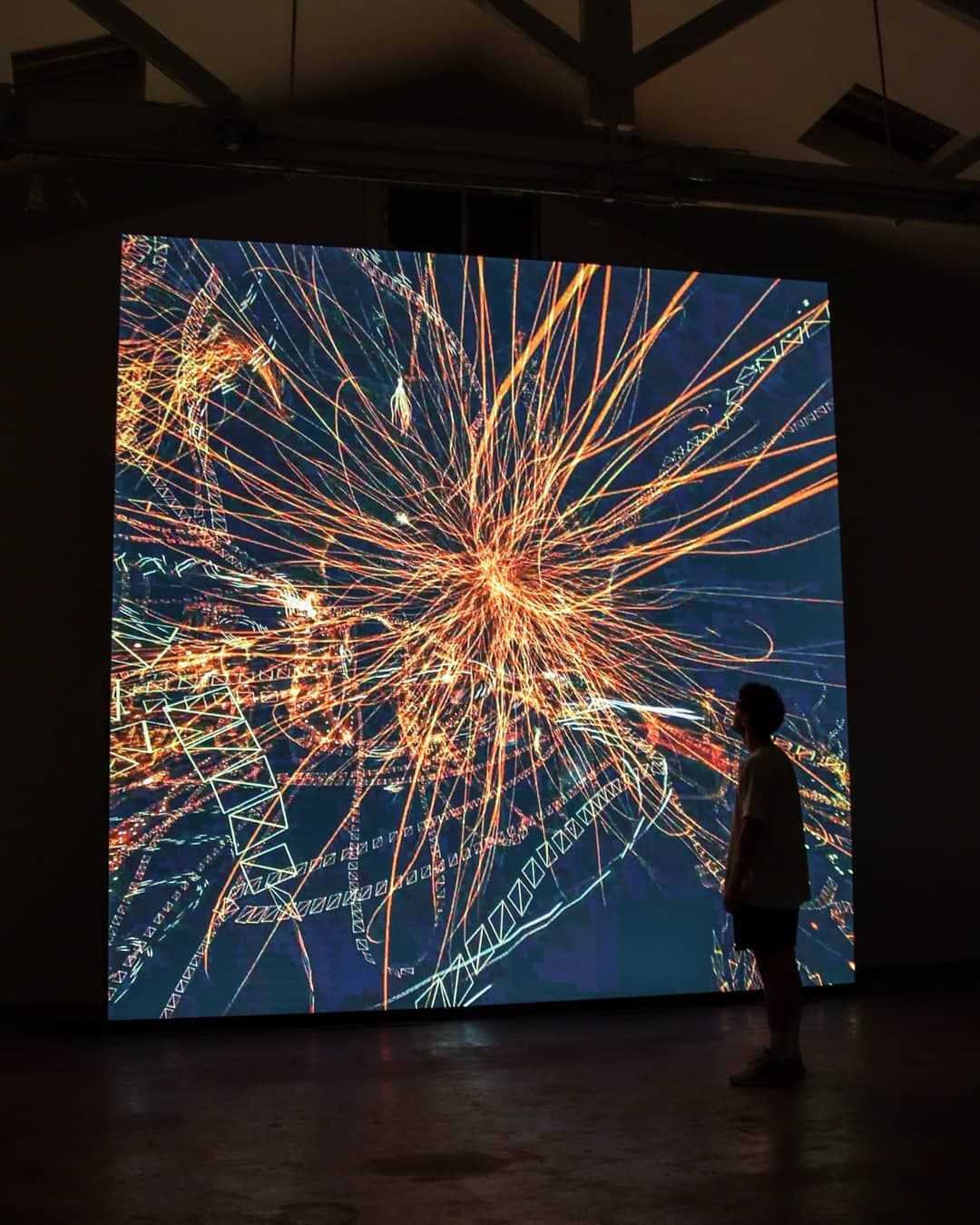 A burst of light threads scattering outward, a visitor small against the scale