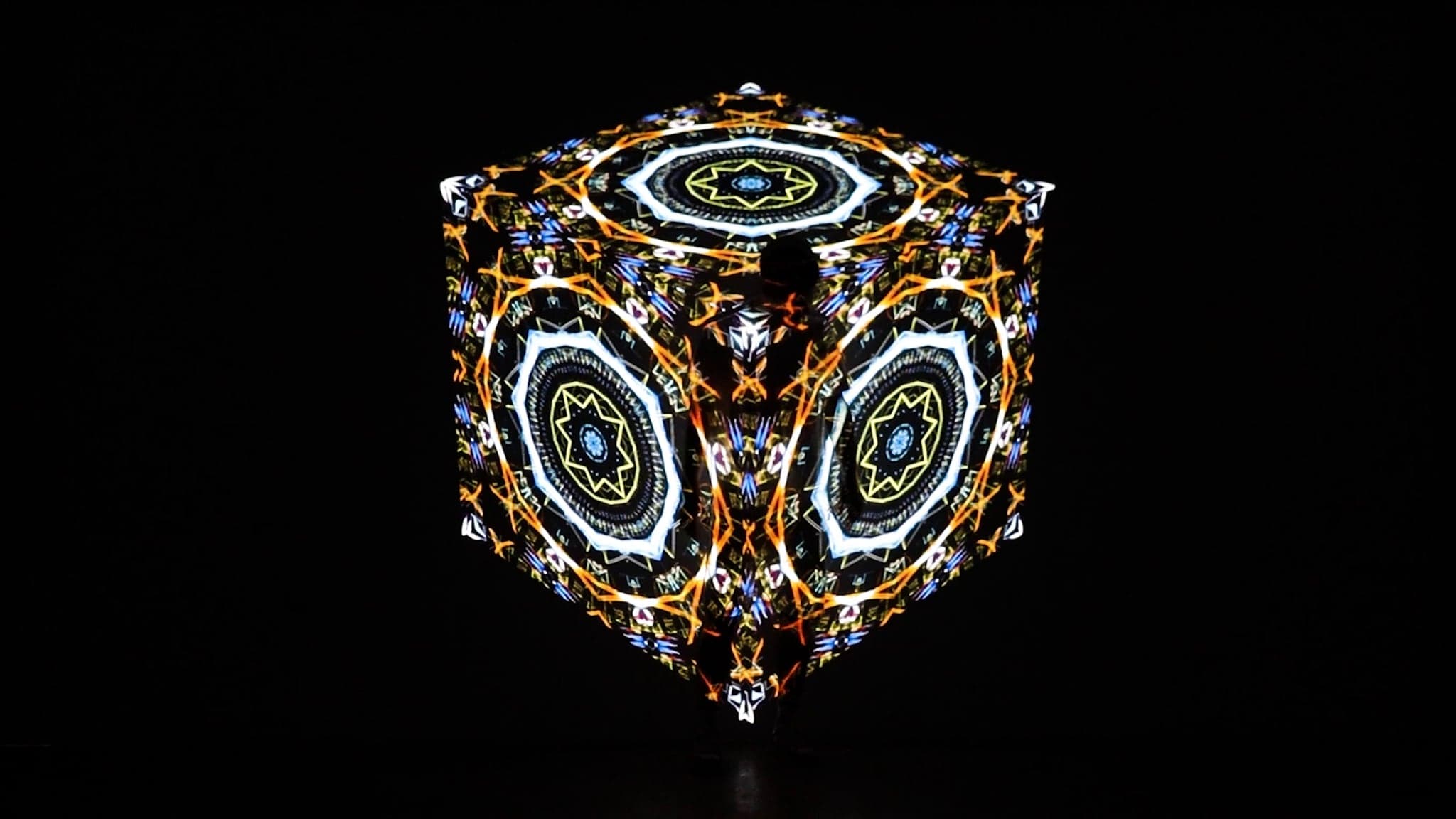 The cube in orange and white filaments, its three visible faces each carrying a different mandala