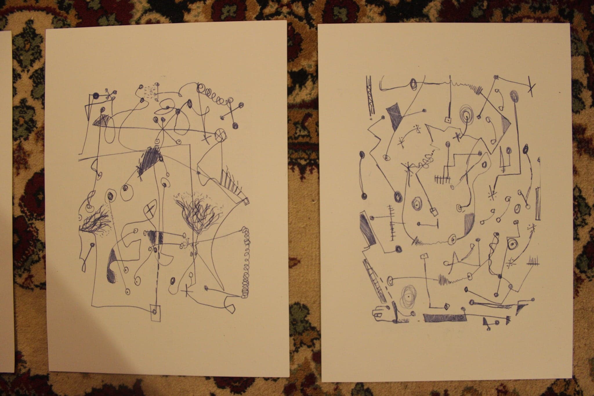 Two large sheets of cream paper side by side, each covered in a continuous blue ink line drawing with small filled shapes