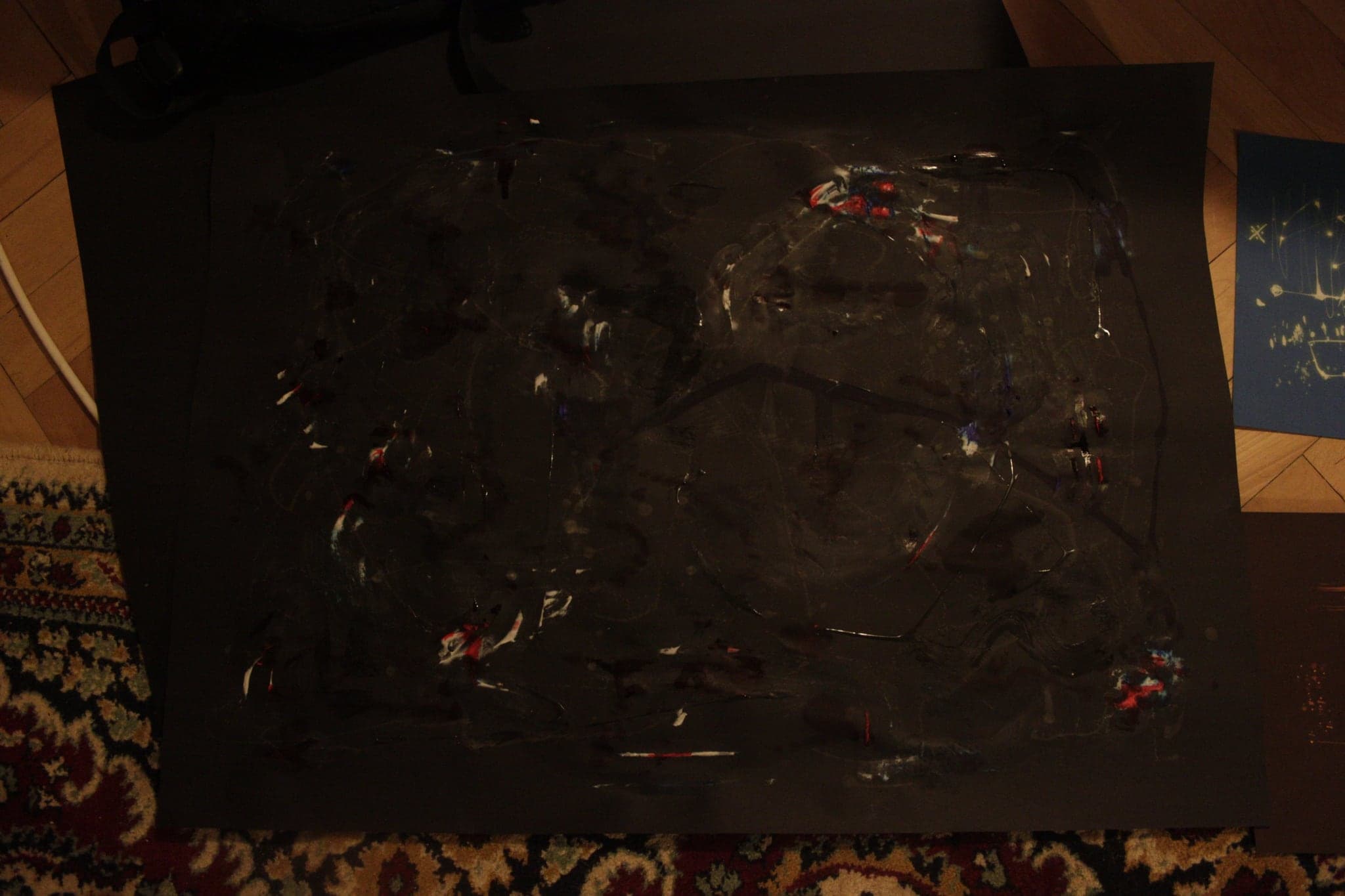 A large black sheet lying on the floor, its surface thick and tarry with small bright flecks caught in it