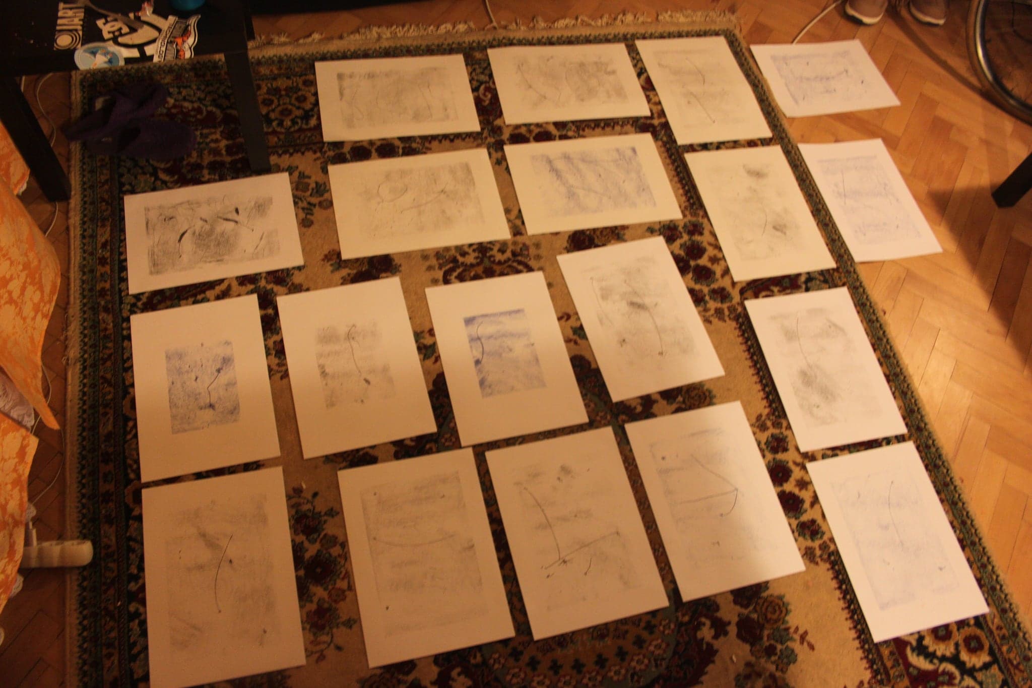 The same set of drawings rearranged, spread further across the parquet floor and photographed from a different angle