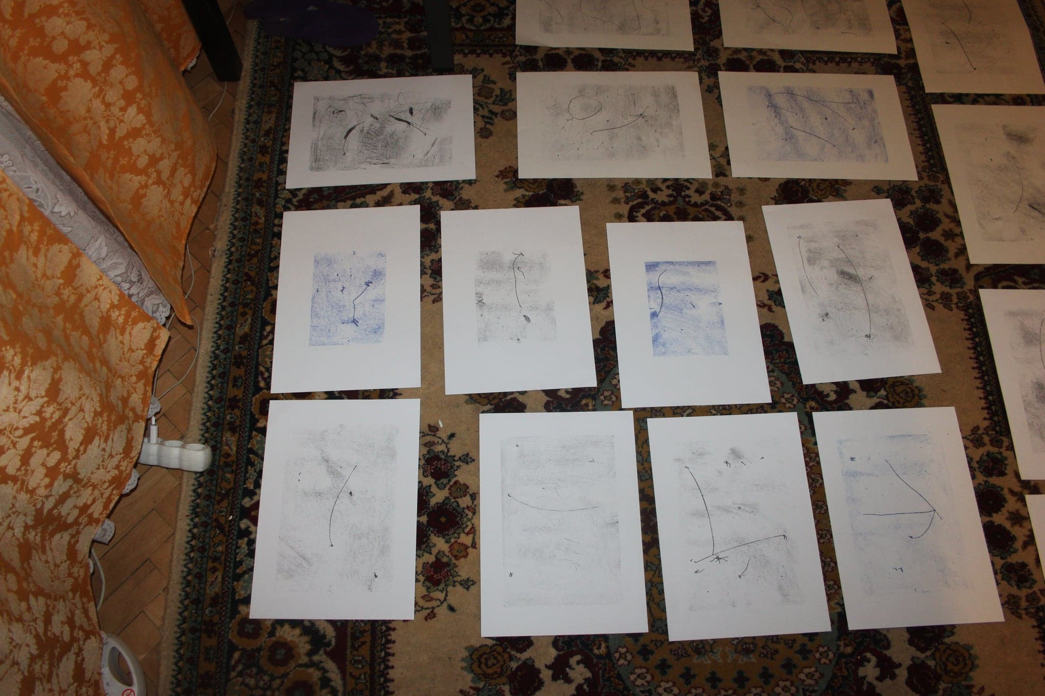 Drawings laid out in rows where four blue ink sheets sit among a larger group of grey graphite drawings