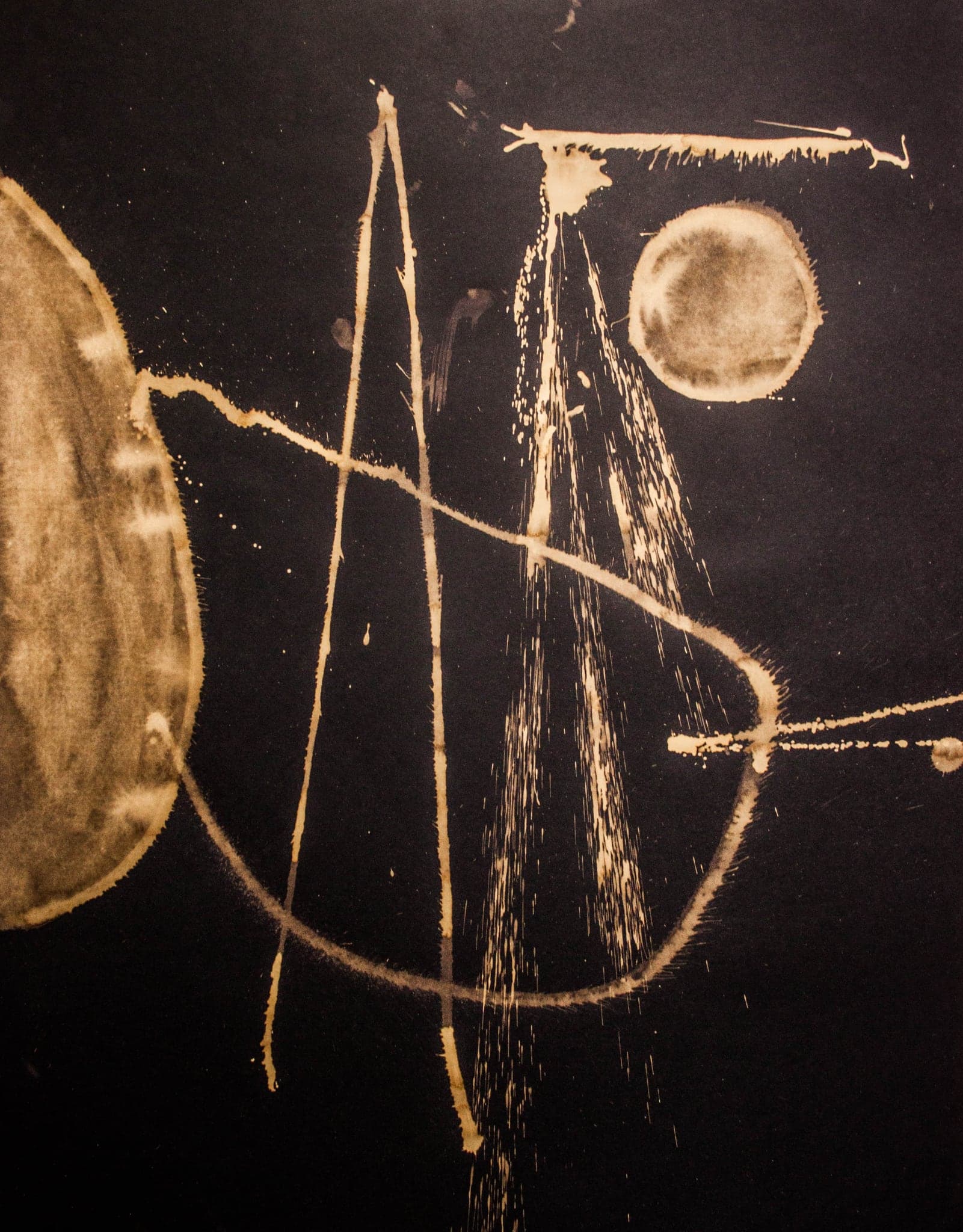 A pale disc at the left edge, tall vertical strokes rising beside it and a smaller bright disc at the top right, on near-black paper