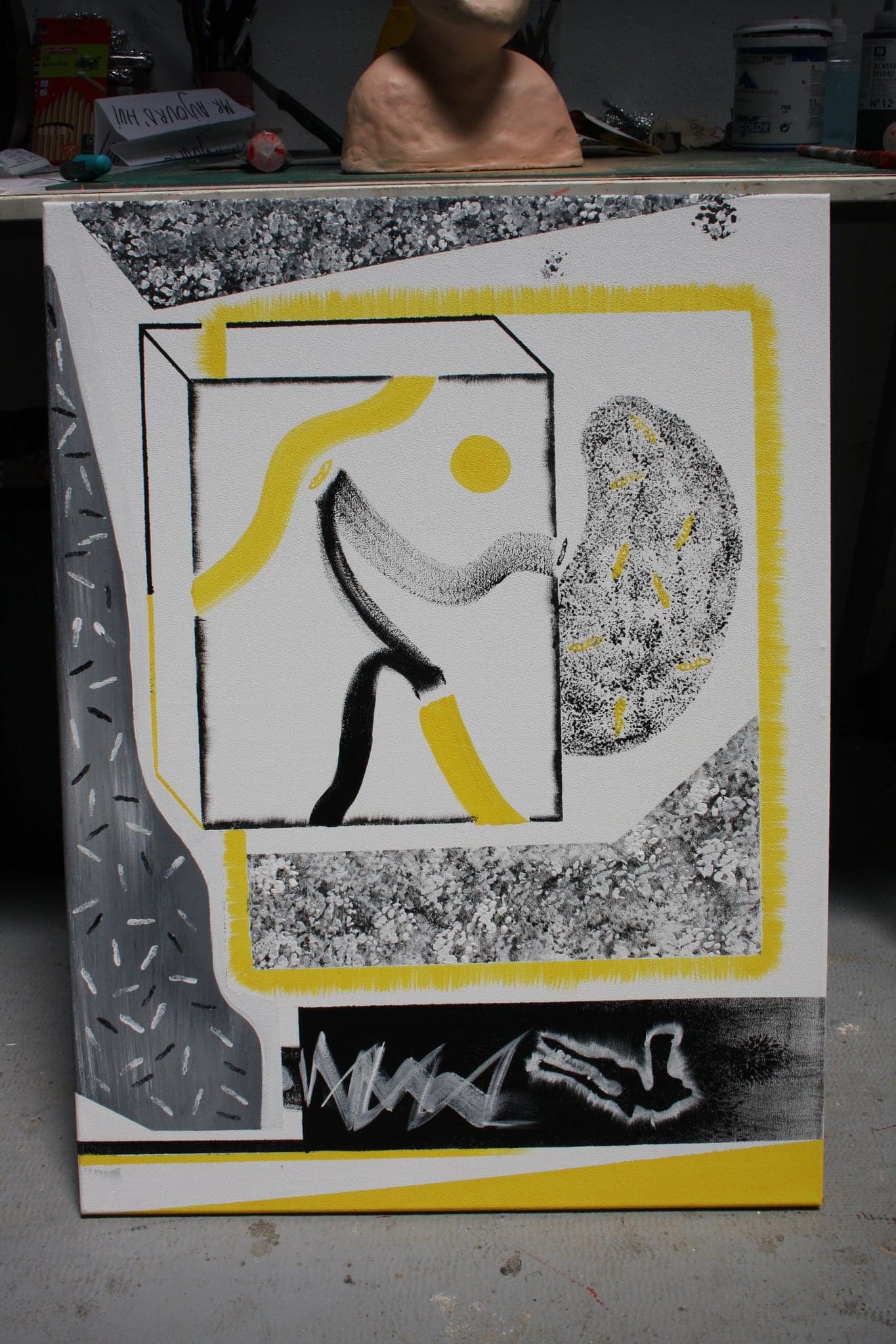 The upright canvas standing on a studio floor in front of a work table, a moulded head resting on the bench behind it.