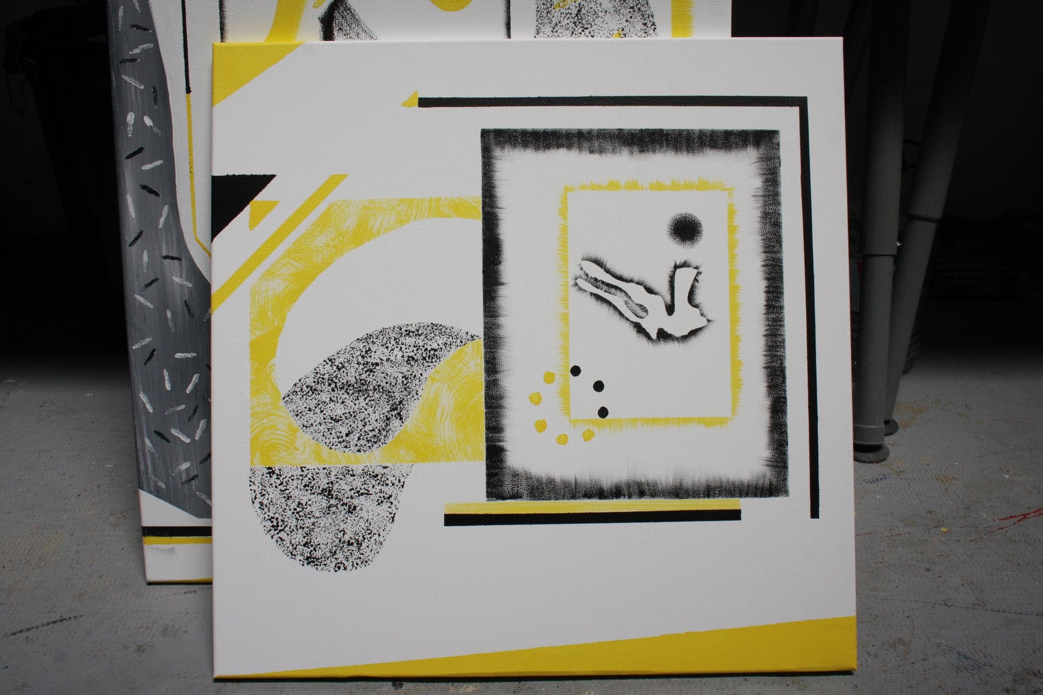 A second canvas from the set on the studio floor, its mark held inside a soft dark frame with yellow at the edges.