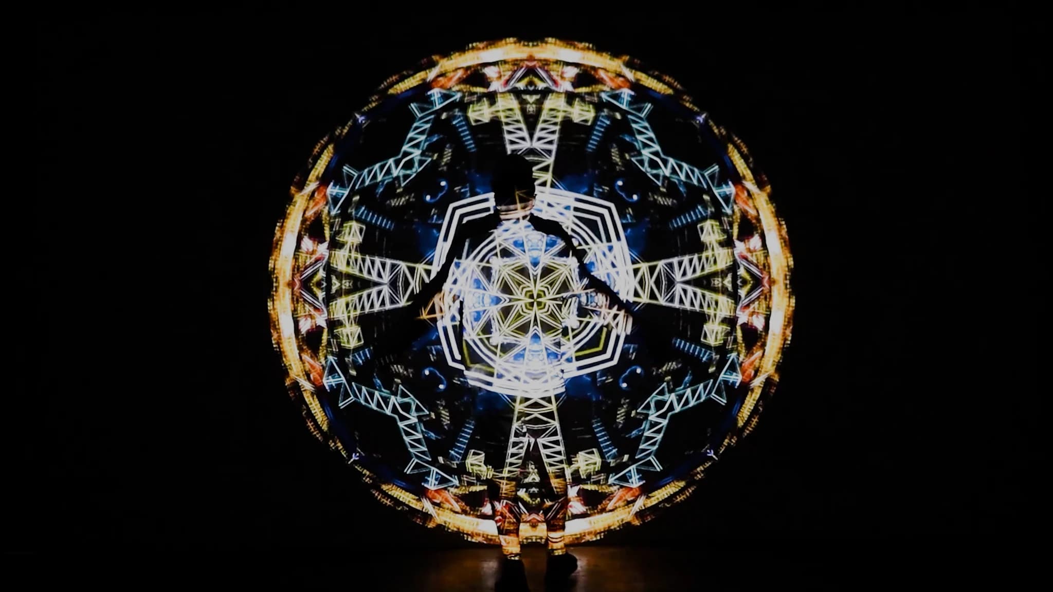 A circular projected mandala of gold and blue light on a black wall, dense with folded geometry