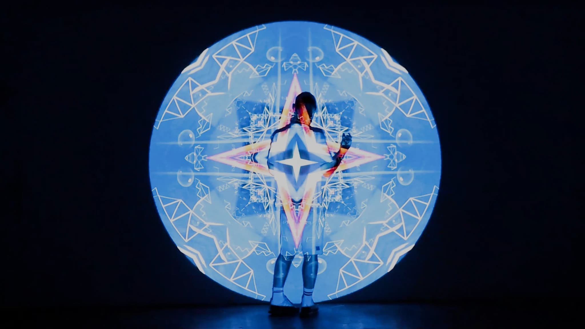 A person standing inside the projected disc, silhouetted at the centre of a pale blue mandala