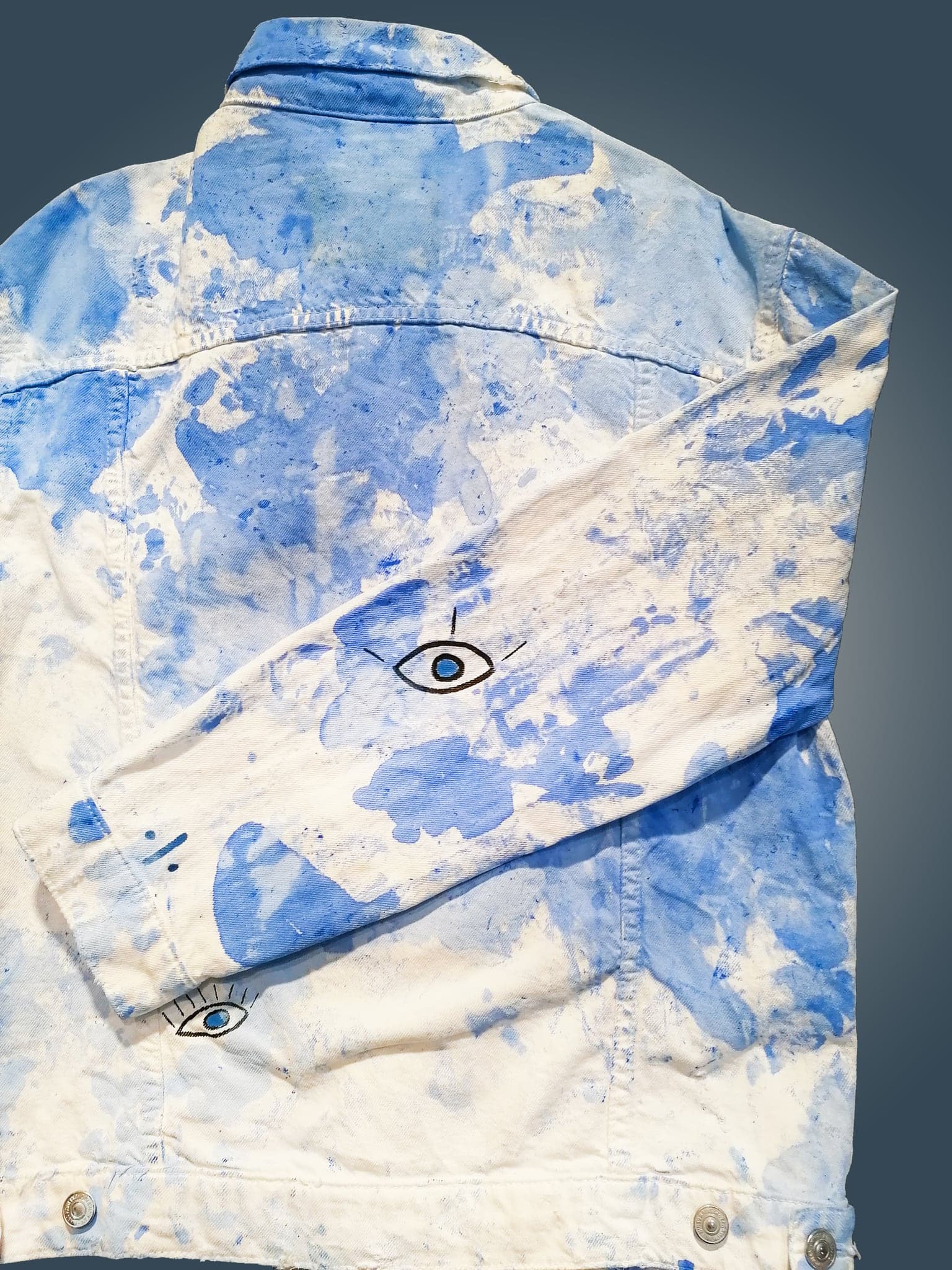 The jacket folded, a small black eye inked into one of the pale gaps near the shoulder