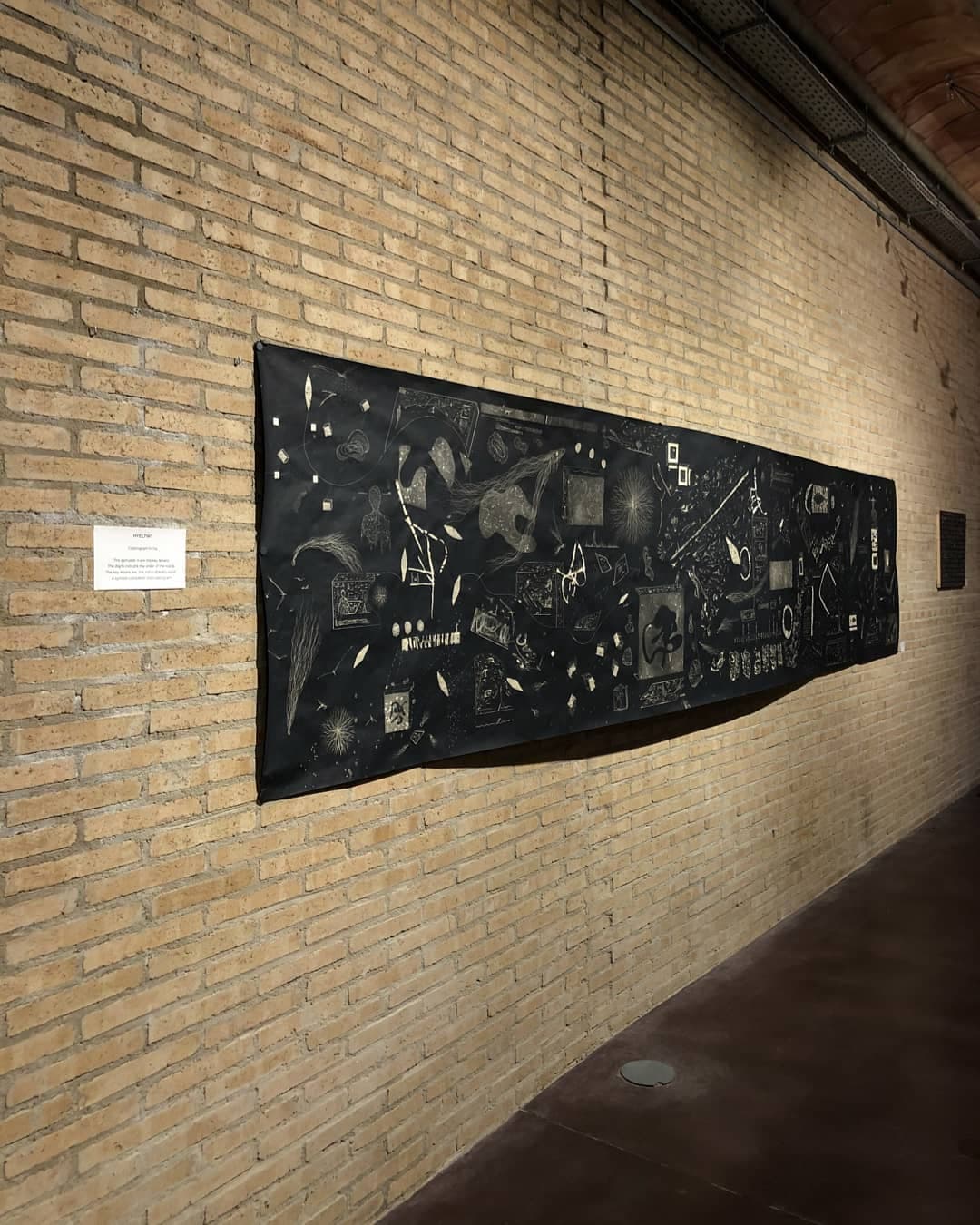 The five-metre panel hung flat along a bare sand-coloured brick wall in a long room, a small printed label to its left