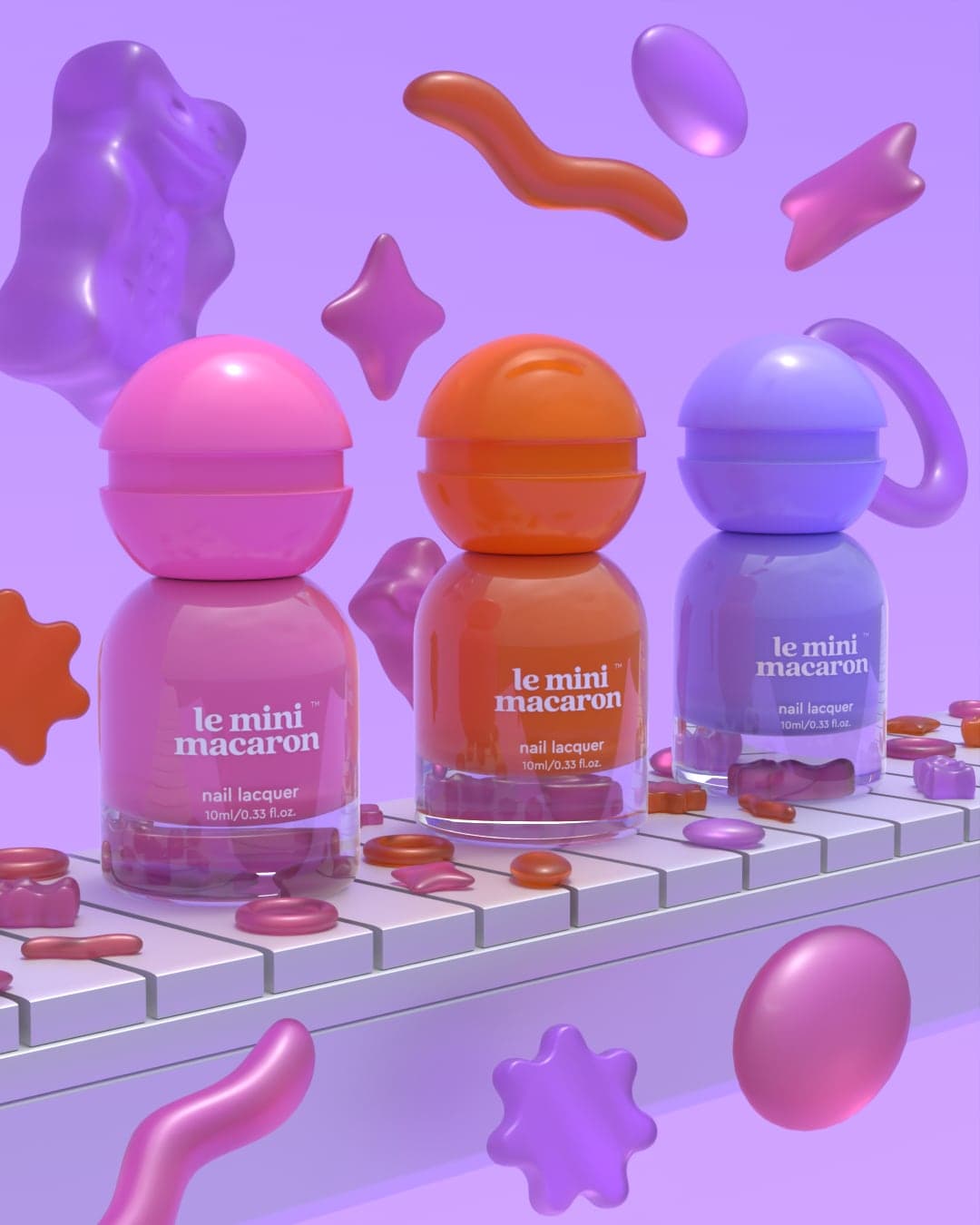 Three nail lacquer bottles — pink, orange and blue, each with a round dome cap — standing on a white belt, with oversized gummy worms, stars and rings floating around them.