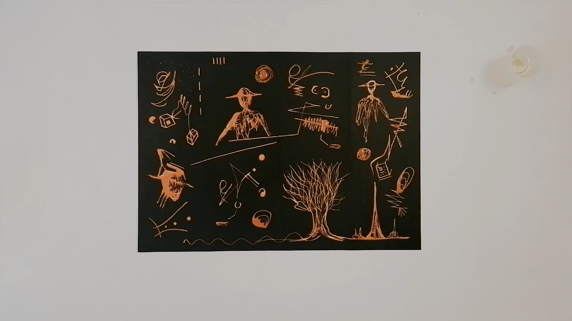 The finished black paper panel seen flat from above on a white table, covered in pale copper bleach drawings: a bird-headed figure, a bare tree, a standing man, a hand holding a cube, and a wavy line along the bottom edge.