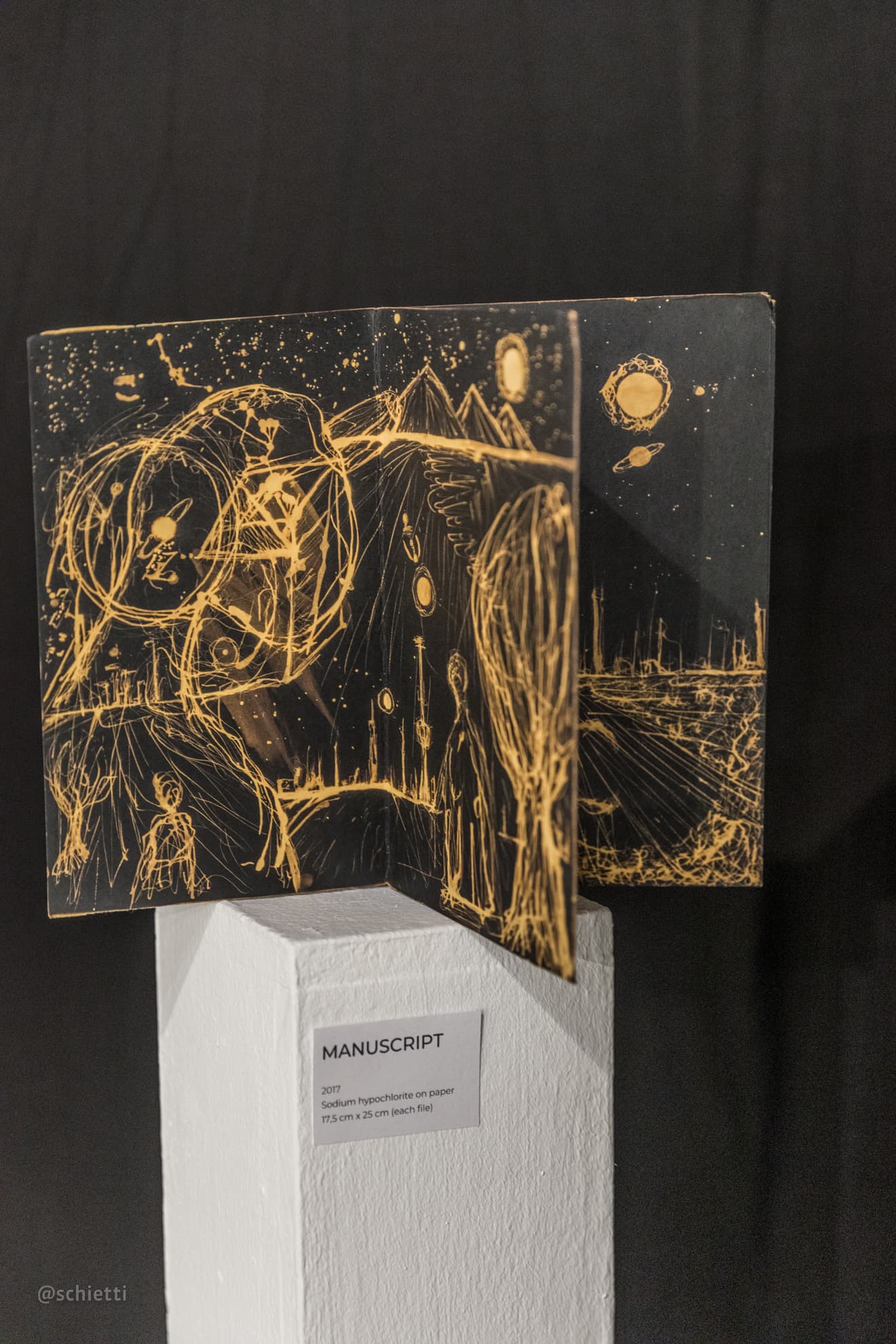 A folded black panel standing open on a white plinth, drawn in pale gold with a horse, a figure and a sun, its wall label below