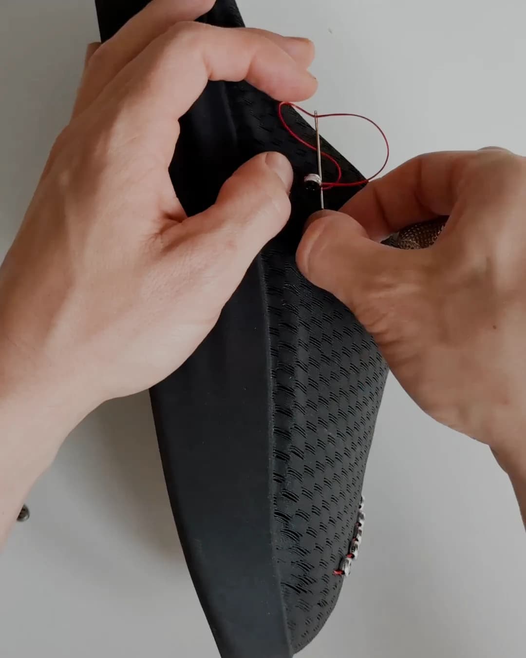 Two hands pressing a metal stud through the printed weave of the upper