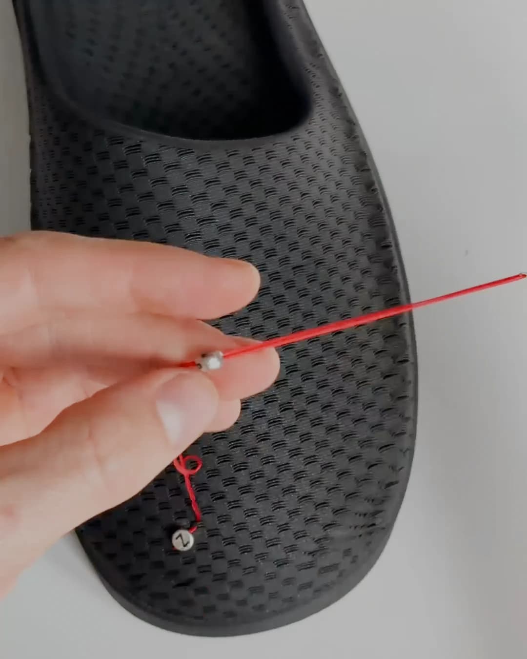 A hand drawing a length of red thread through a needle above the black shoe