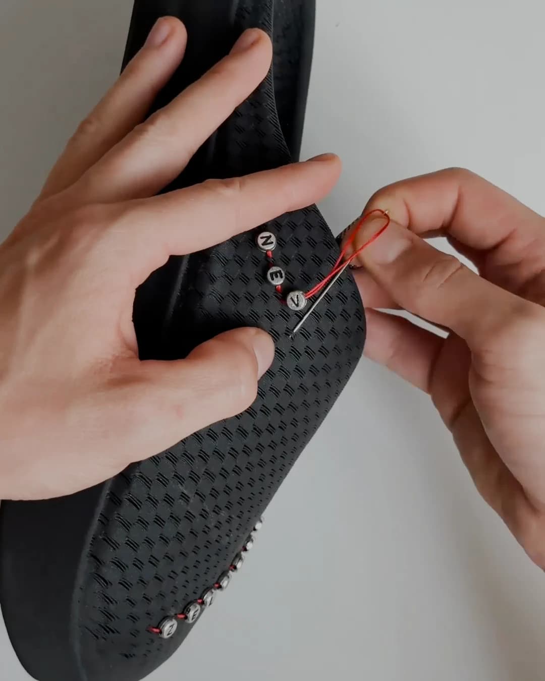 The row of lettered beads part-sewn along the side of the shoe, red thread running between them