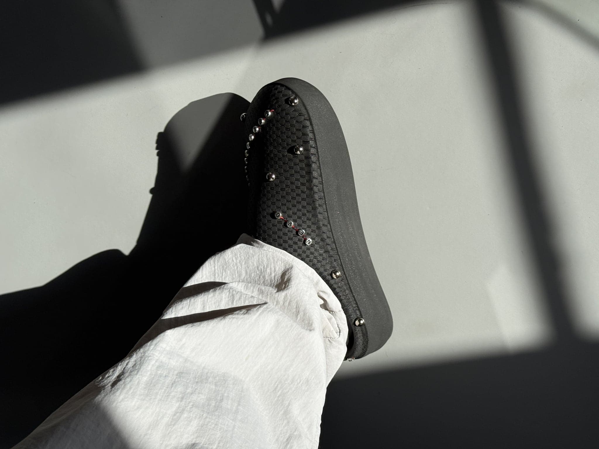 The shoe worn in strong directional light, a hard shadow cutting across the foot and the studded flank