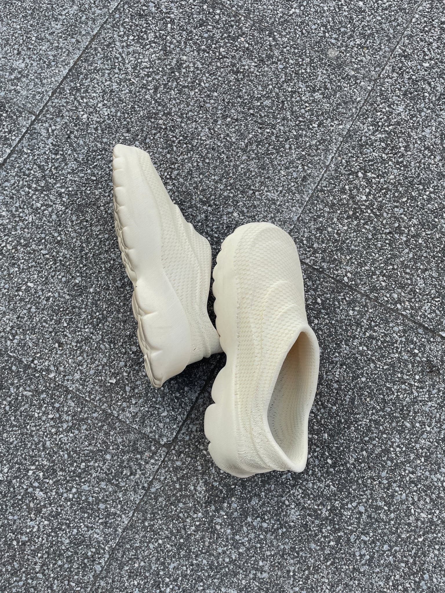 A bone-white pair of the finished shoes lying on dark speckled granite paving, one on its side showing the ridged sole edge.