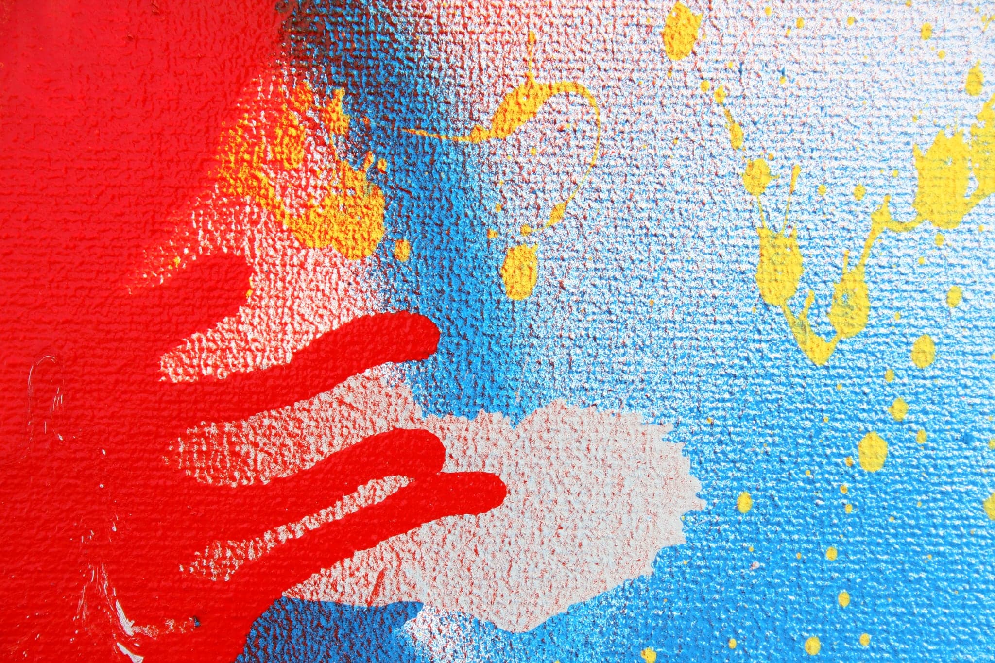 Close view: red fingers reaching across blue, yellow flecks scattered over it.