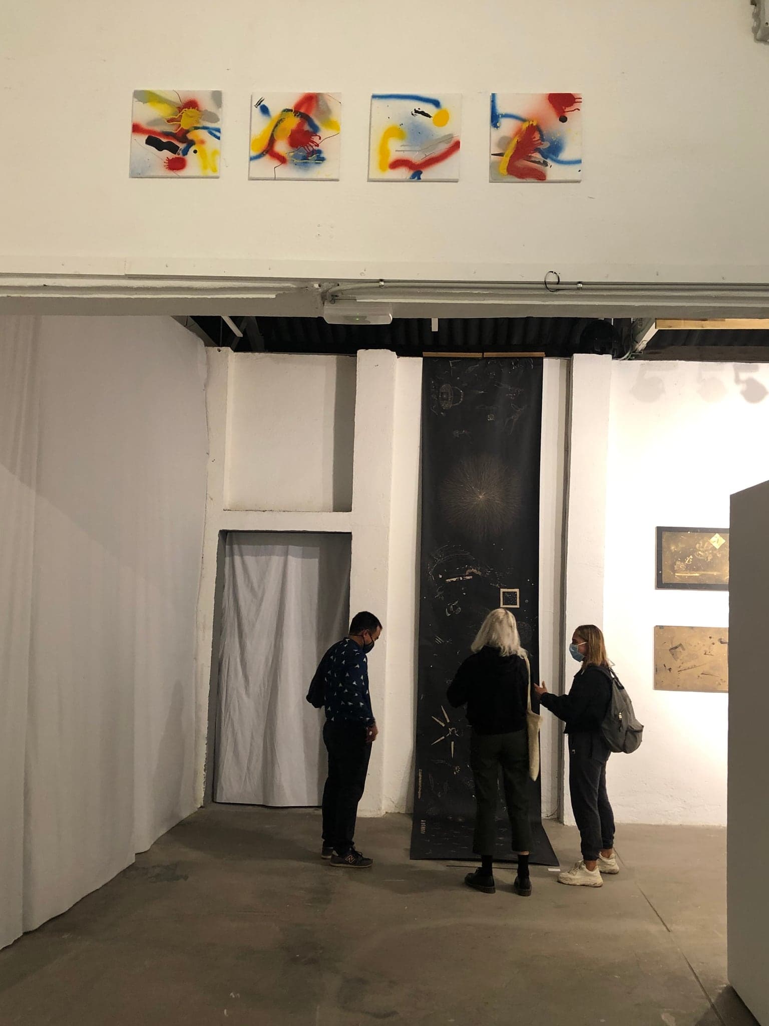 The four small spray-painted squares hung in a row high above a doorway, bright against the white wall