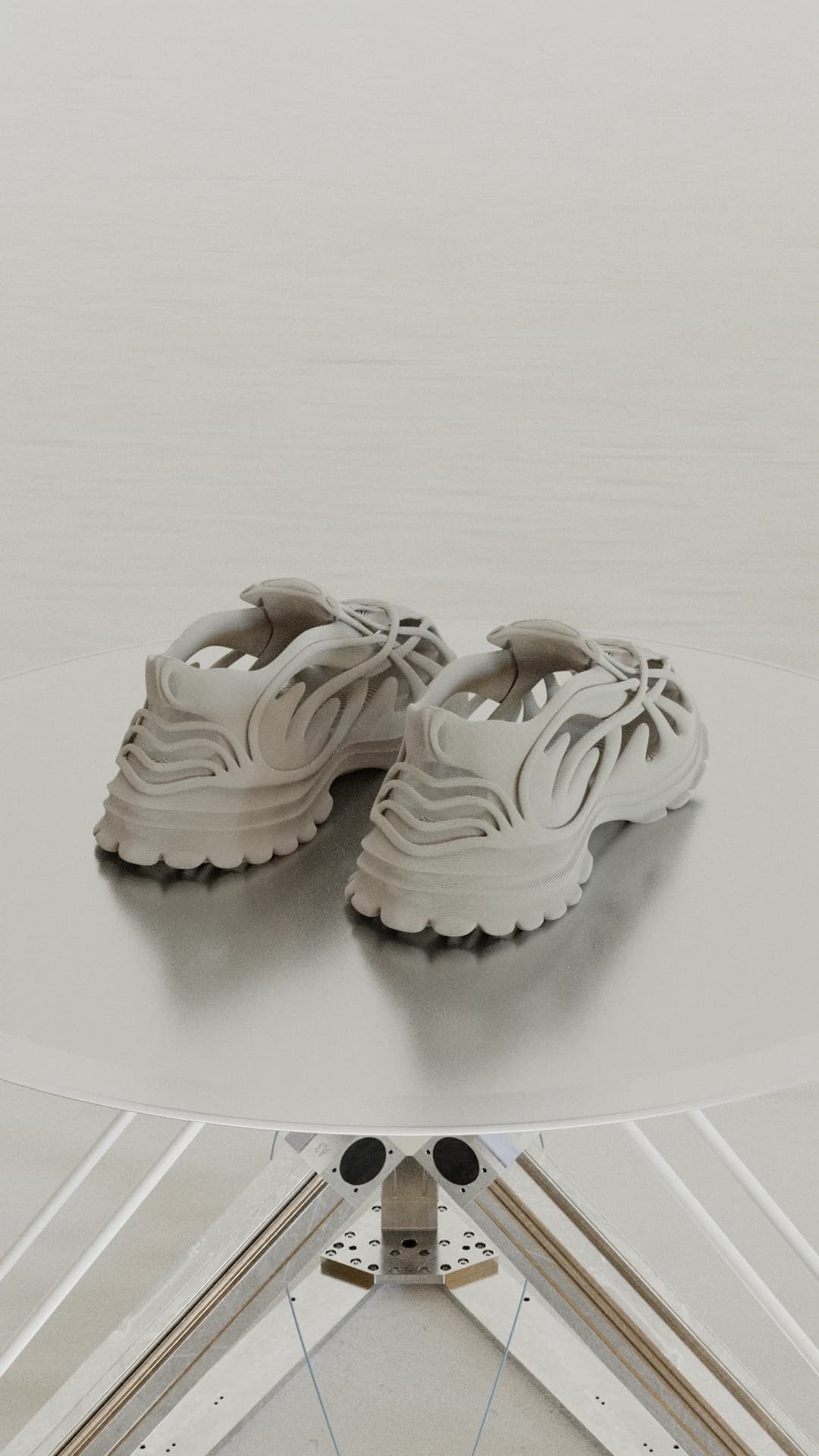 A pair of the shoes in an off-white printed finish, seen from behind on a round turntable above an aluminium rig