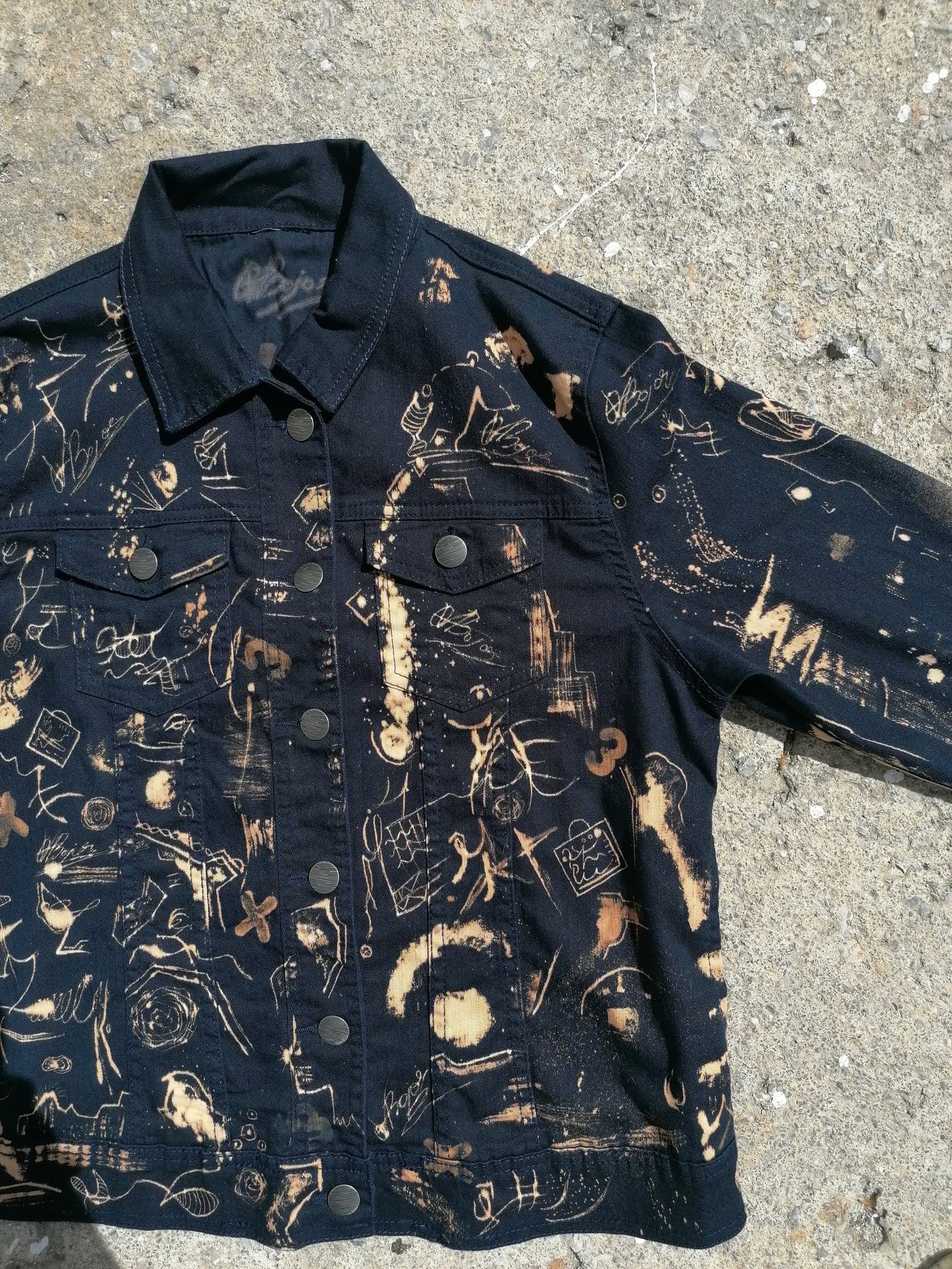 The jacket laid open on concrete in daylight, the marks reading warmer against the stone