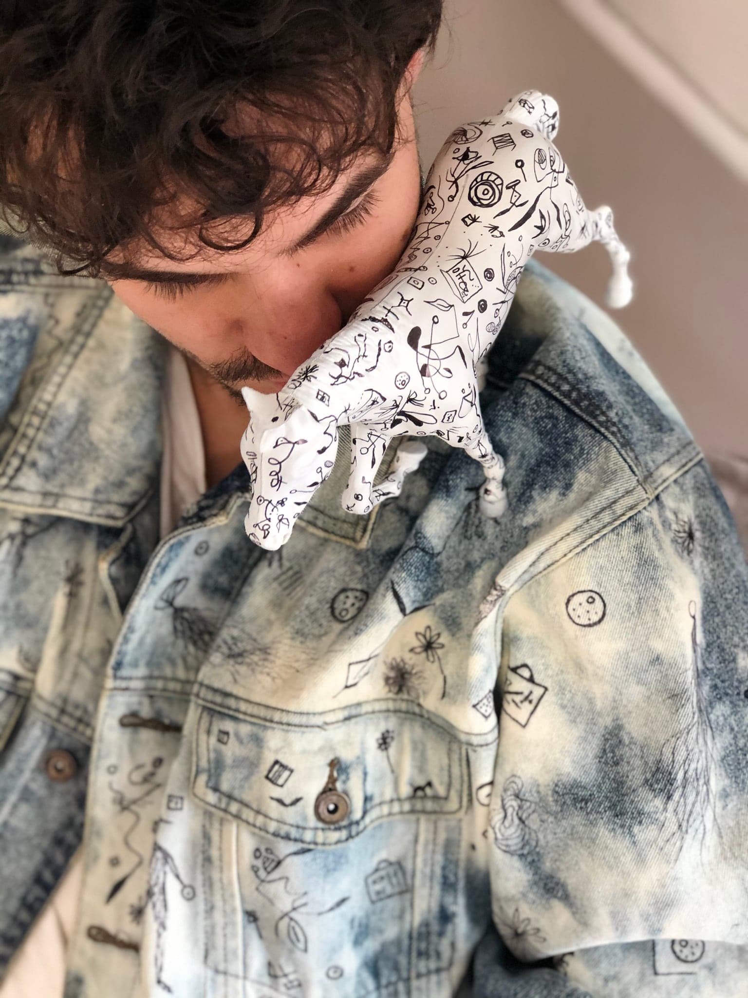 The horse held against the shoulder of the bleached denim jacket, which carries the same drawn marks