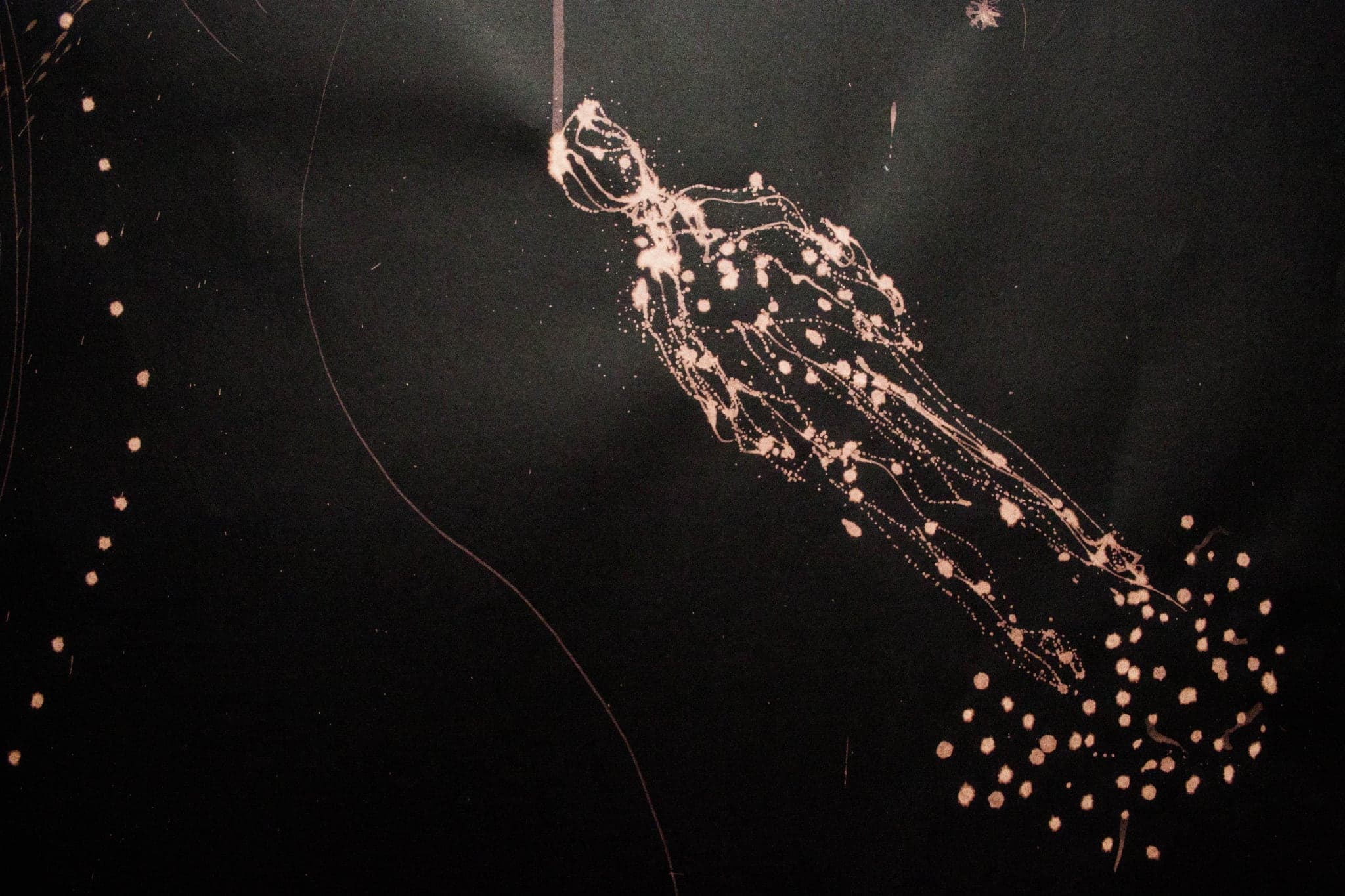 A figure drawn in pale flecks and threads on near-black paper, coming apart along its length and dispersing into a scatter of loose dots at lower right.