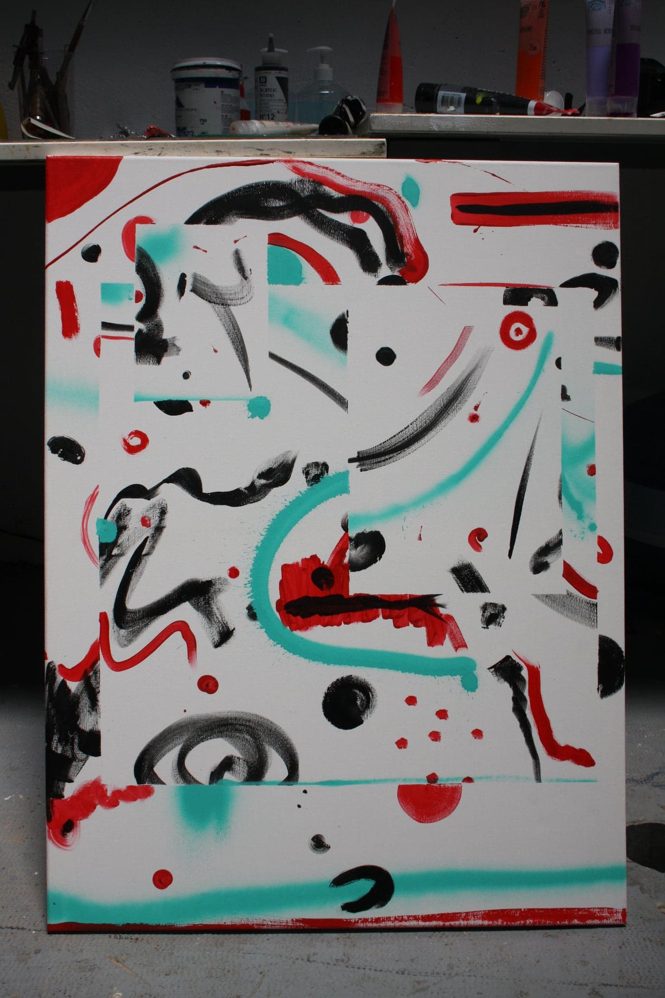 The second canvas on the studio floor, its red, turquoise and black marks running loose across the whole field rather than in bands.