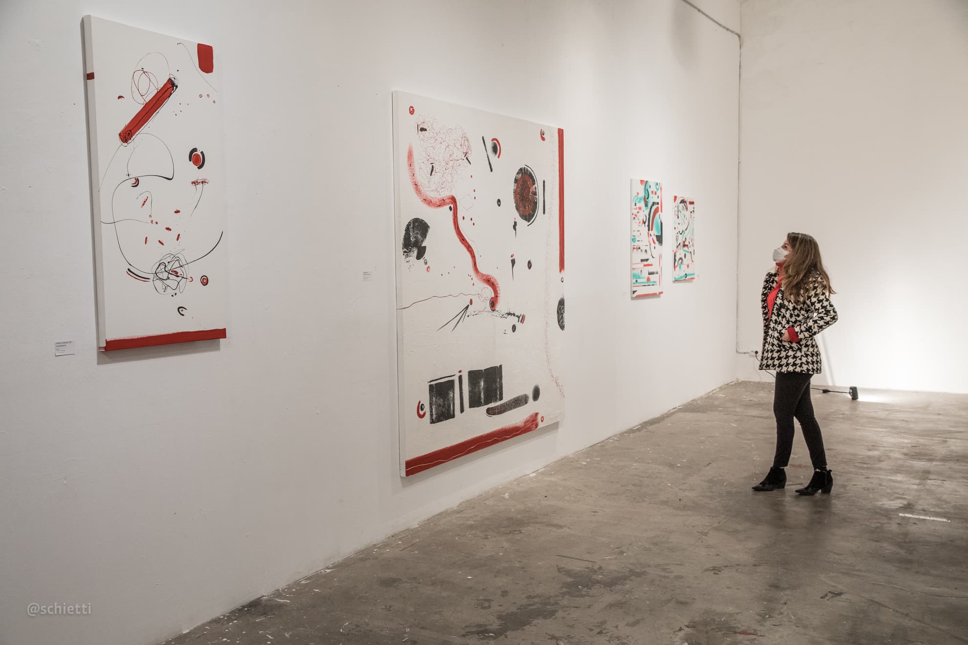 The long gallery wall with three of the white paintings hung in a row and one visitor standing at the far end