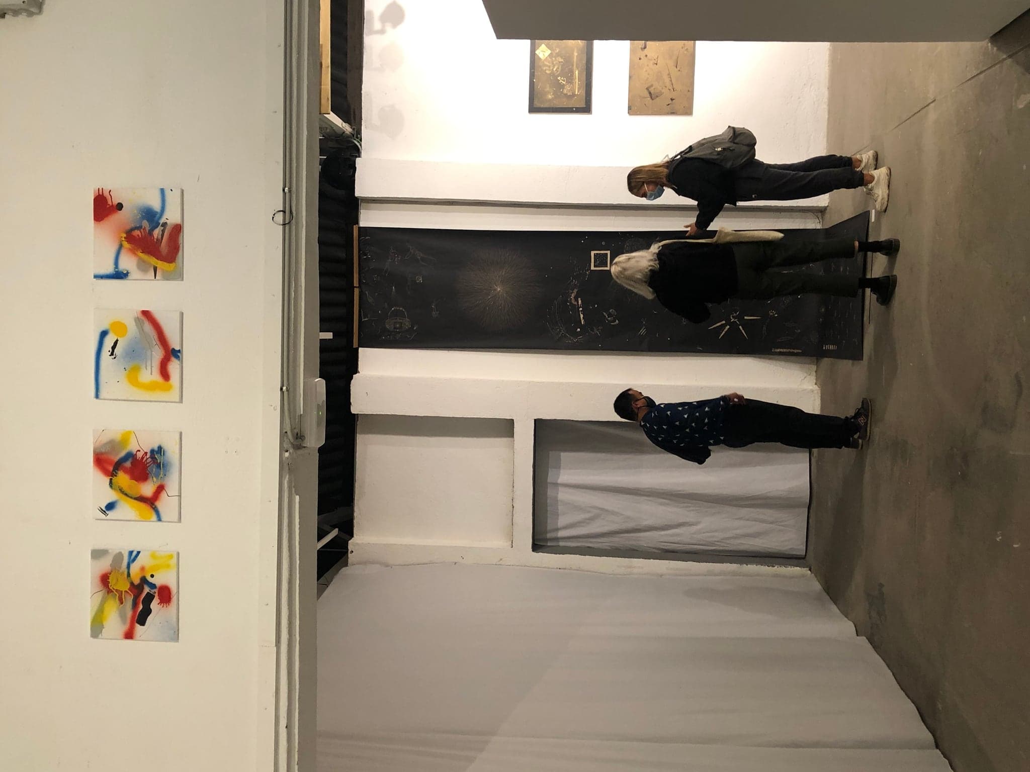 The four small spray-painted squares hung in a row high above a doorway, bright against the white wall