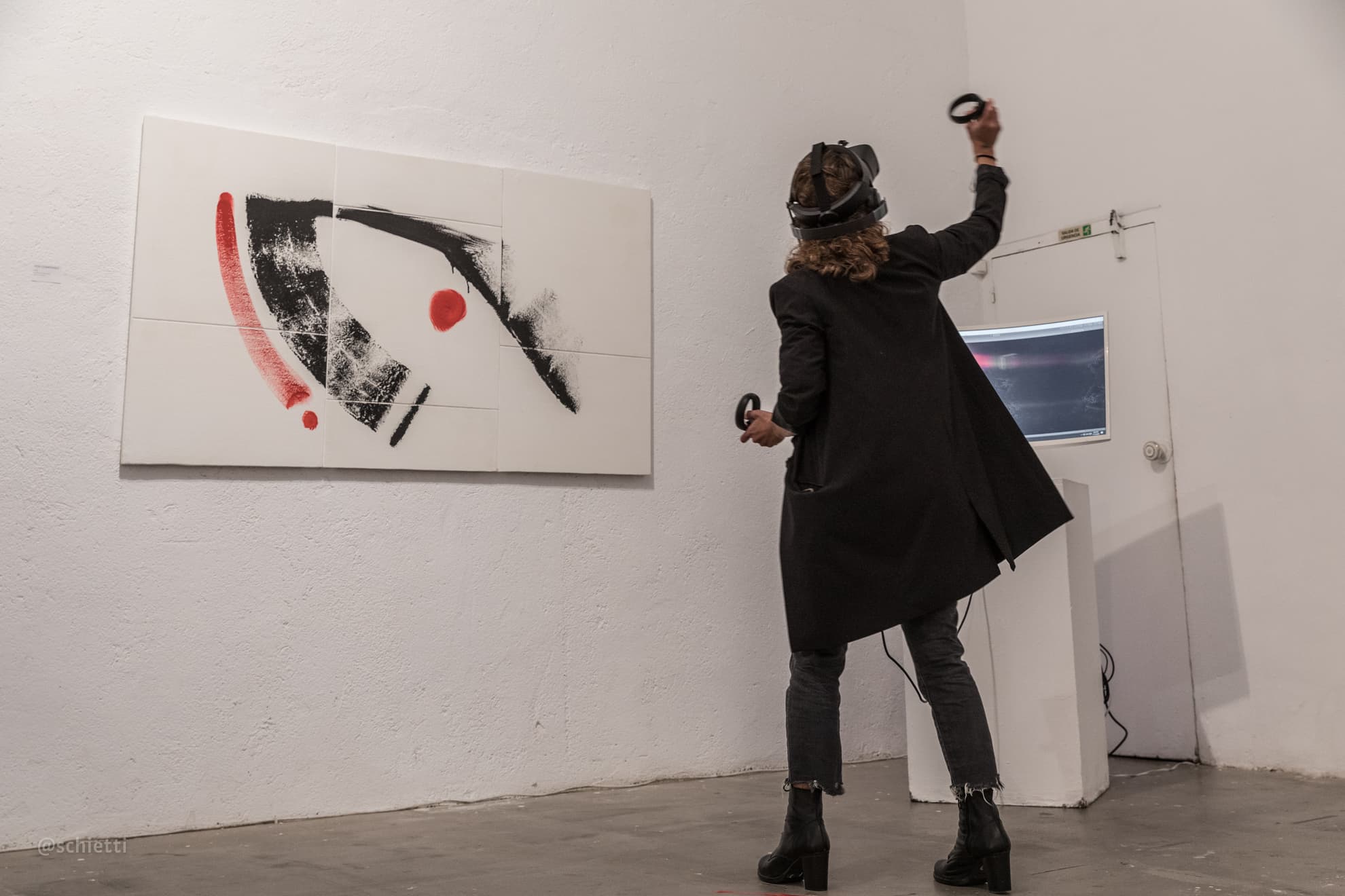 A visitor in a virtual reality headset with controllers raised, standing in front of YOU COMPOSED