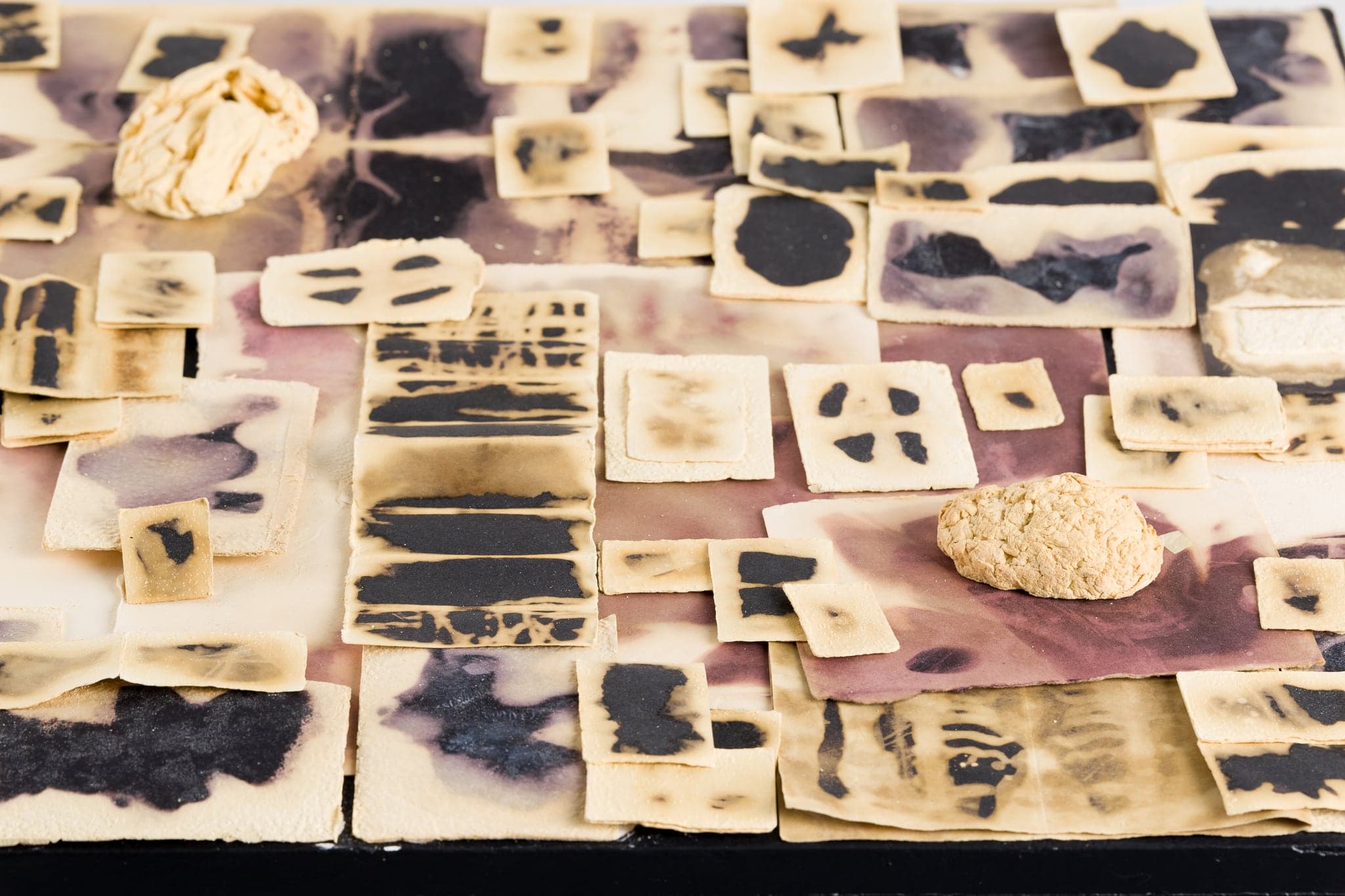 Close view across the tiled top of the plinth, cream wax tiles with black marks receding into shallow focus, two pale crumpled wax lumps among them.