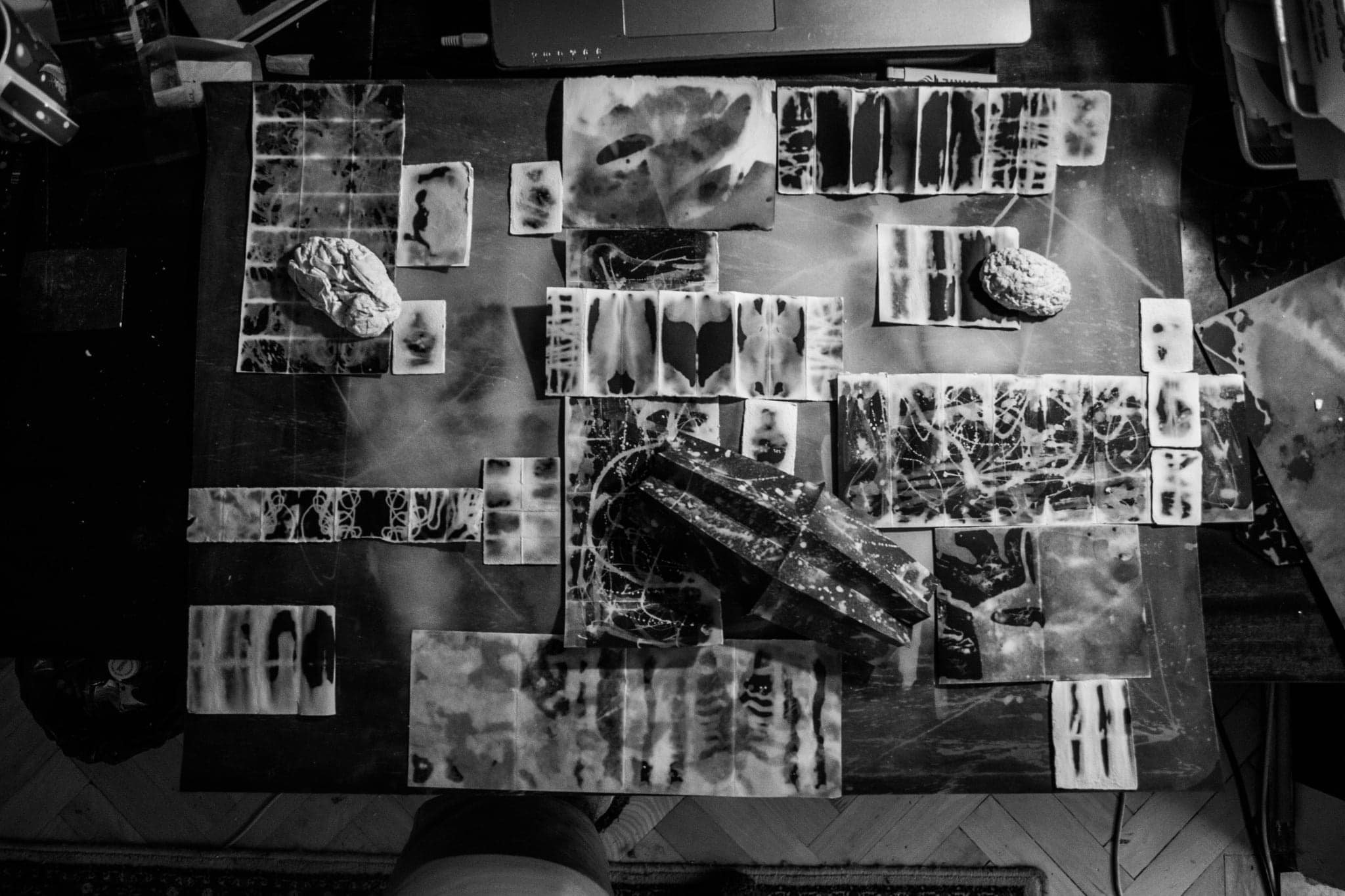 Black and white overhead of the whole arrangement of wax tiles spread across a dark table, a folded dark sheet angled at the centre.