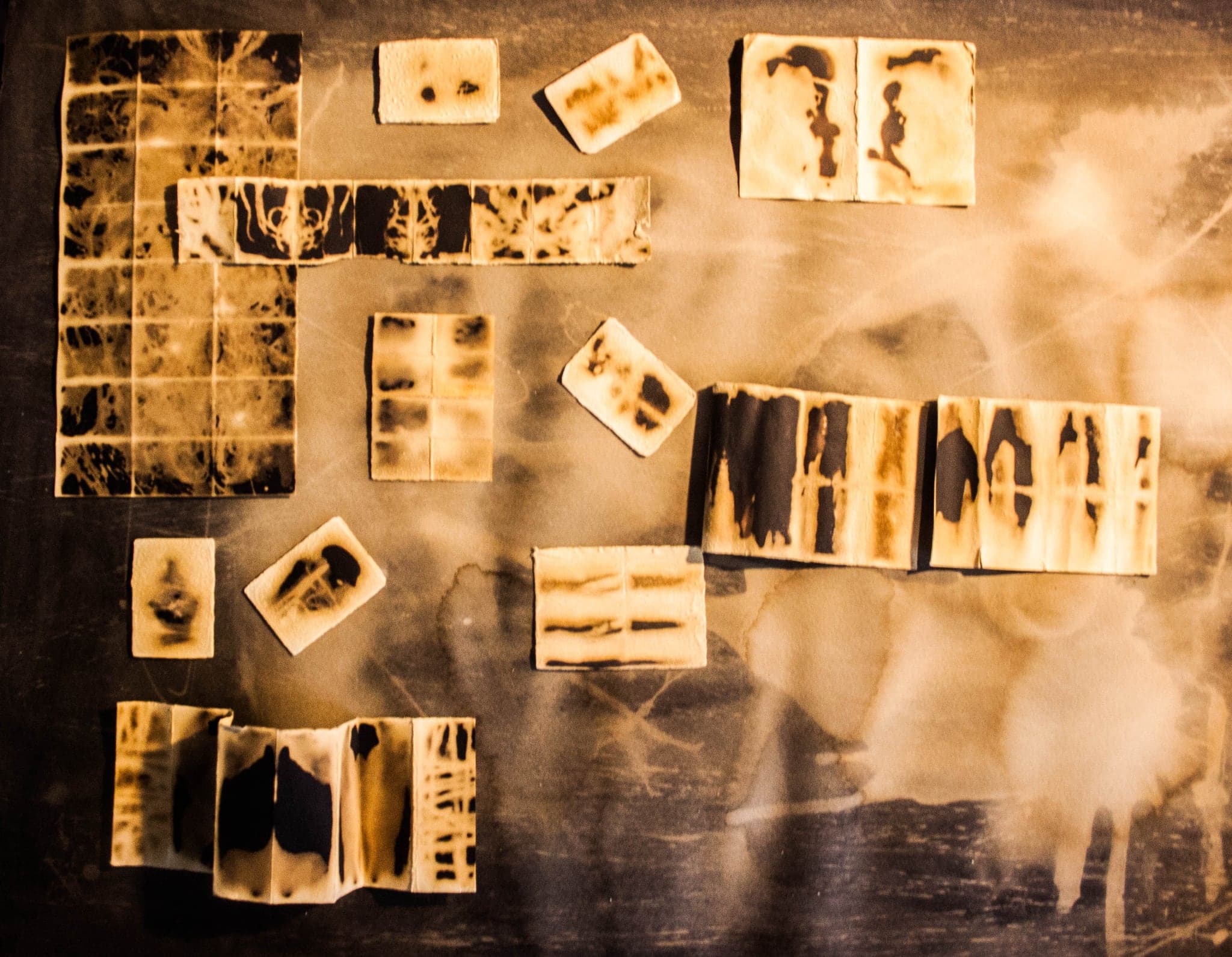 Overhead view of a sparser arrangement of amber wax tiles on a dark ground, each holding black grid-like marks.