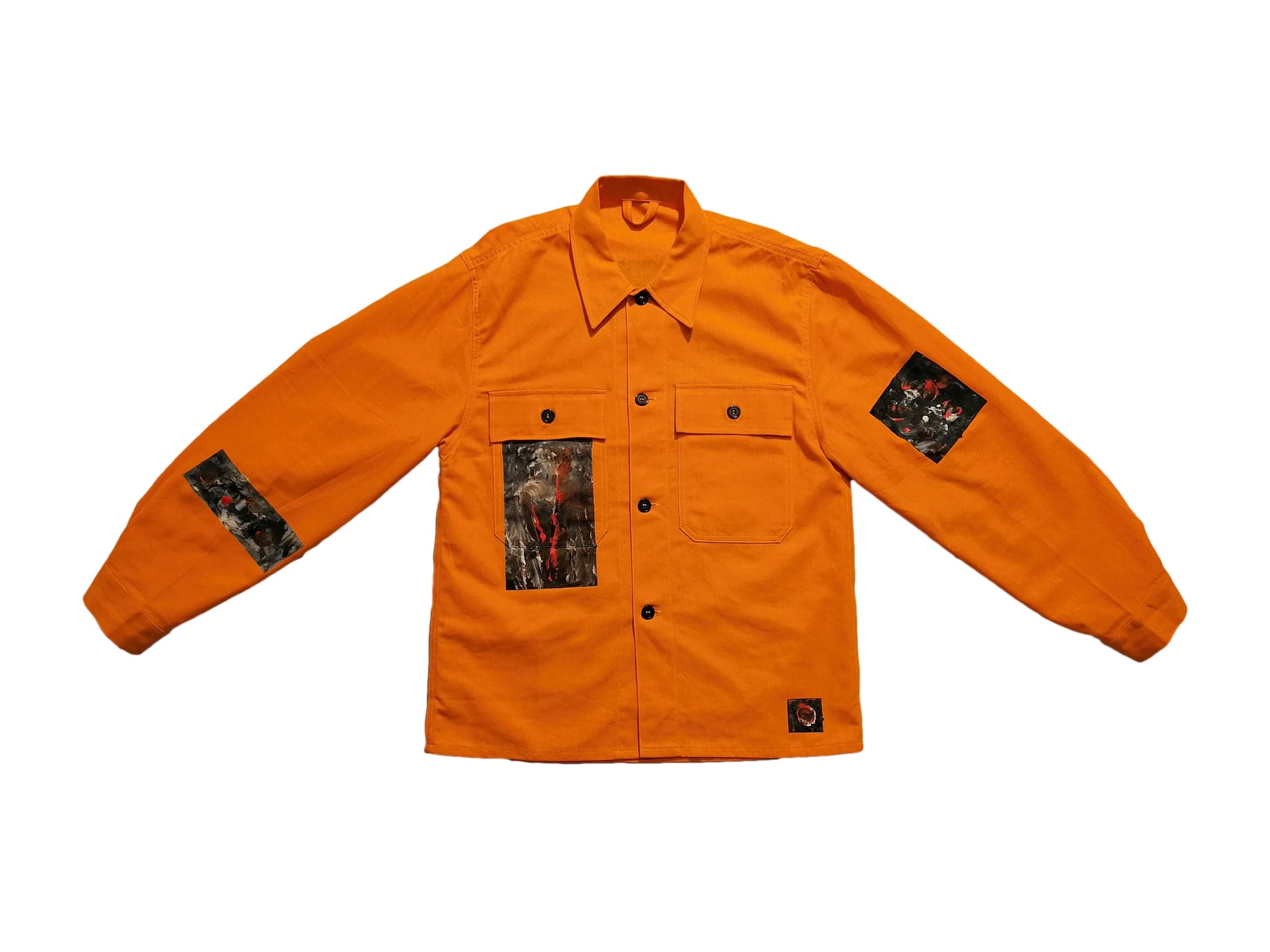 The orange work shirt flat on white, panels of black and white painting sewn to the chest and both sleeves