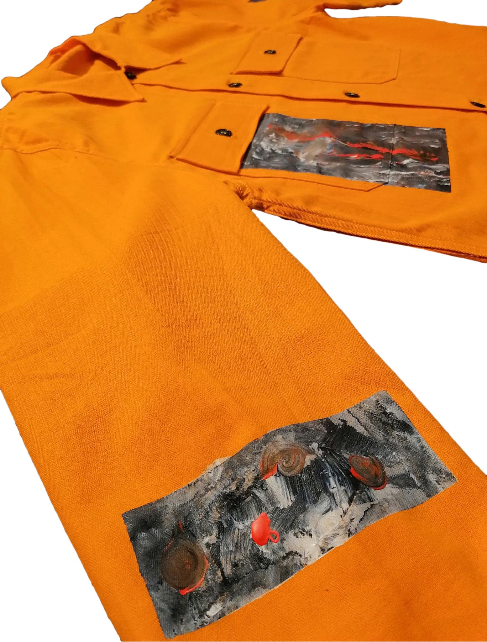 The shirt laid out with two of its panels in frame, the orange drill against the grey painting