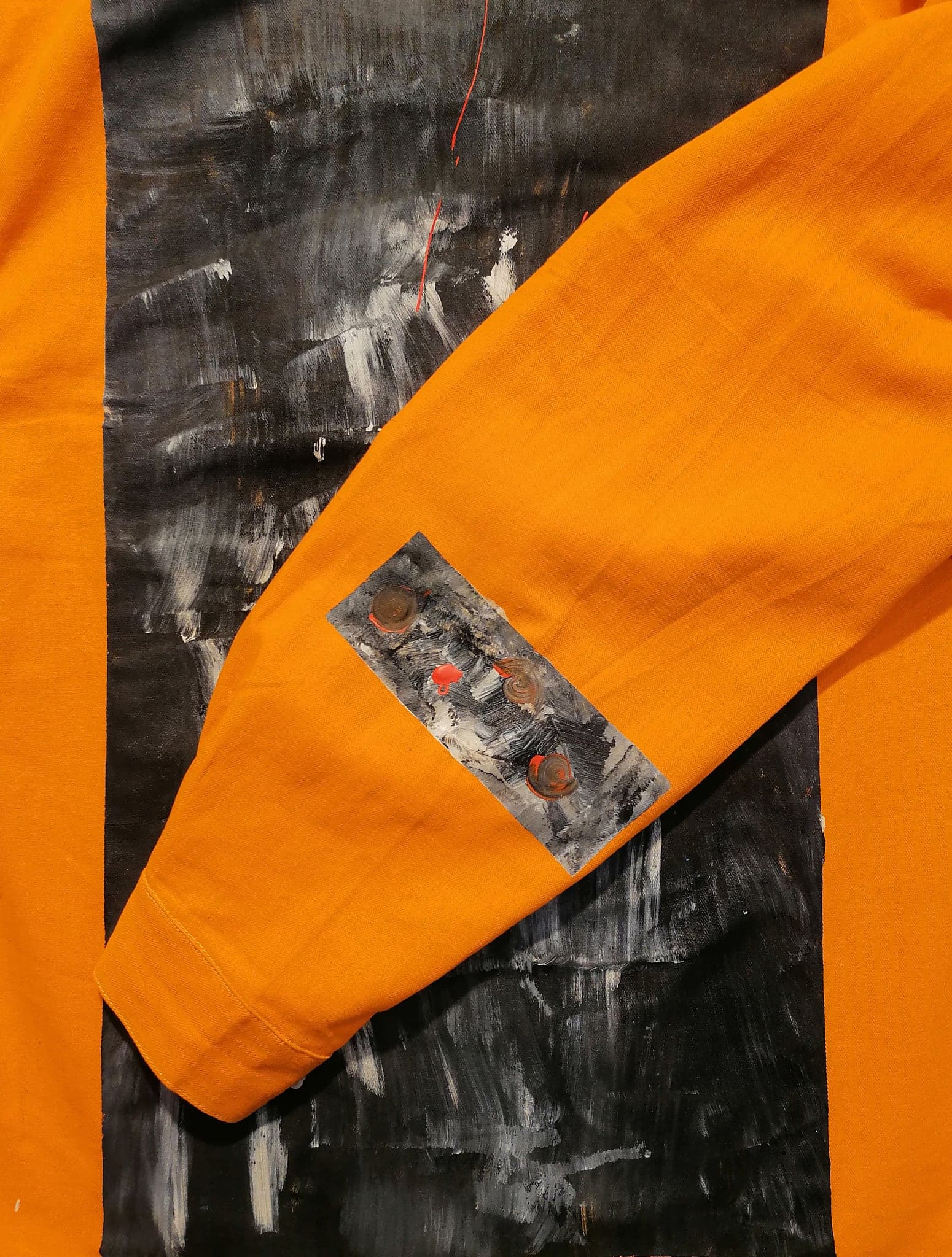 An orange sleeve lying across the black and white painting it was cut into