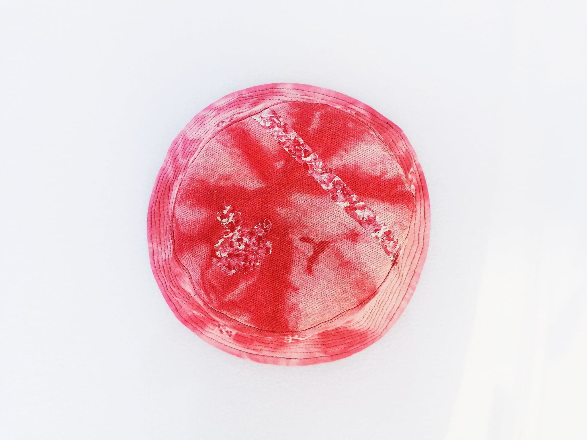 A bucket hat dyed deep red, photographed from directly above on white, with a cluster of thick white paint pressed into the crown