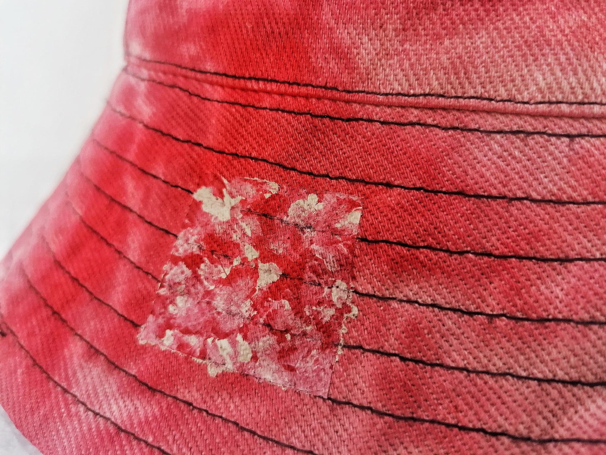Close view of the red hat's twill, the stitched brim lines running across it and a crust of white paint sitting proud of the weave