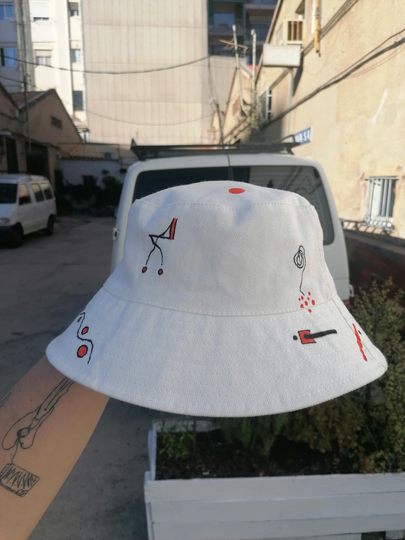 A white bucket hat held up in a street, carrying a small handful of black and red drawn marks