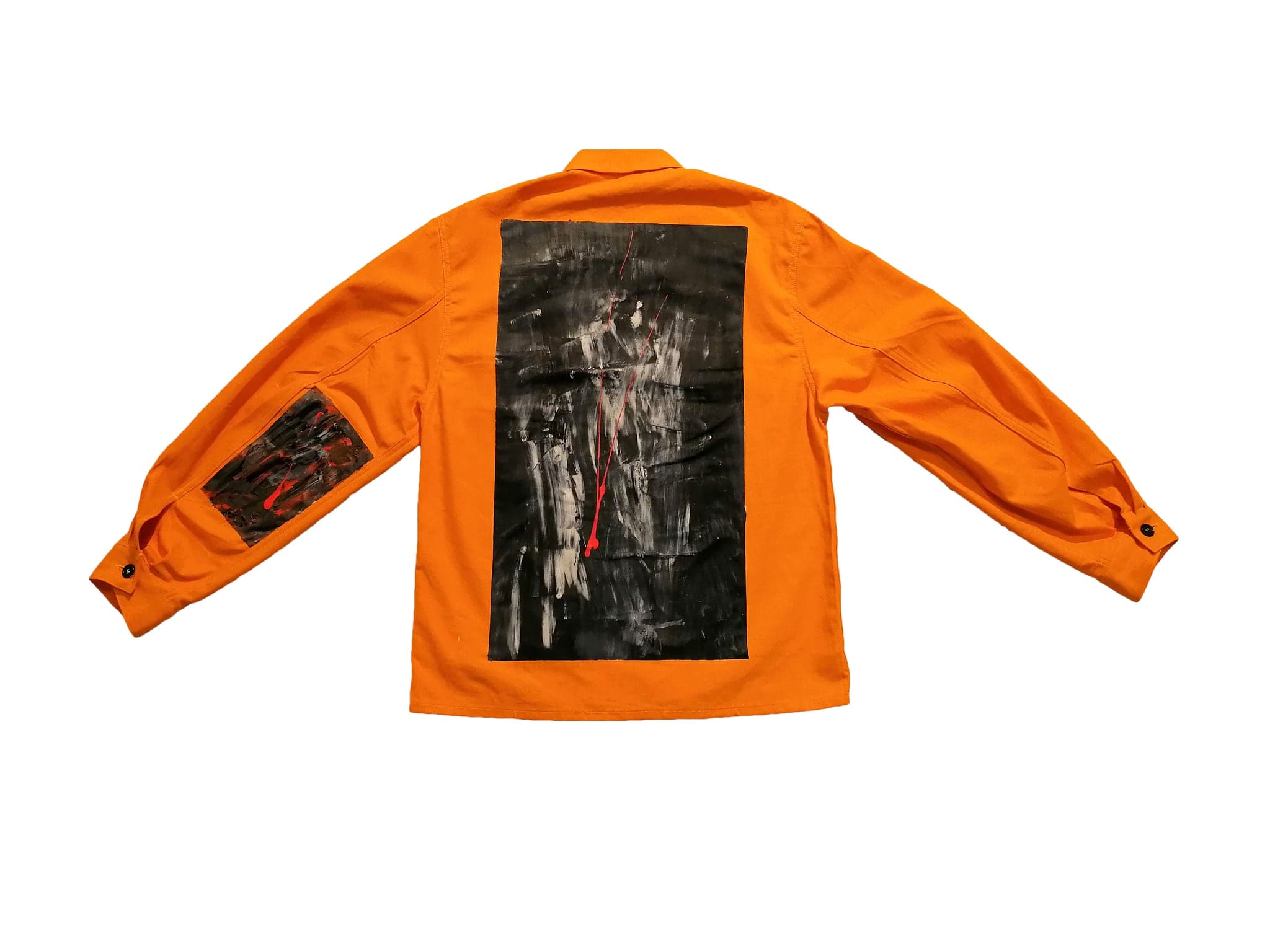 An orange work shirt laid flat on white, a dark painted panel sewn flat onto the back and a smaller one on the sleeve