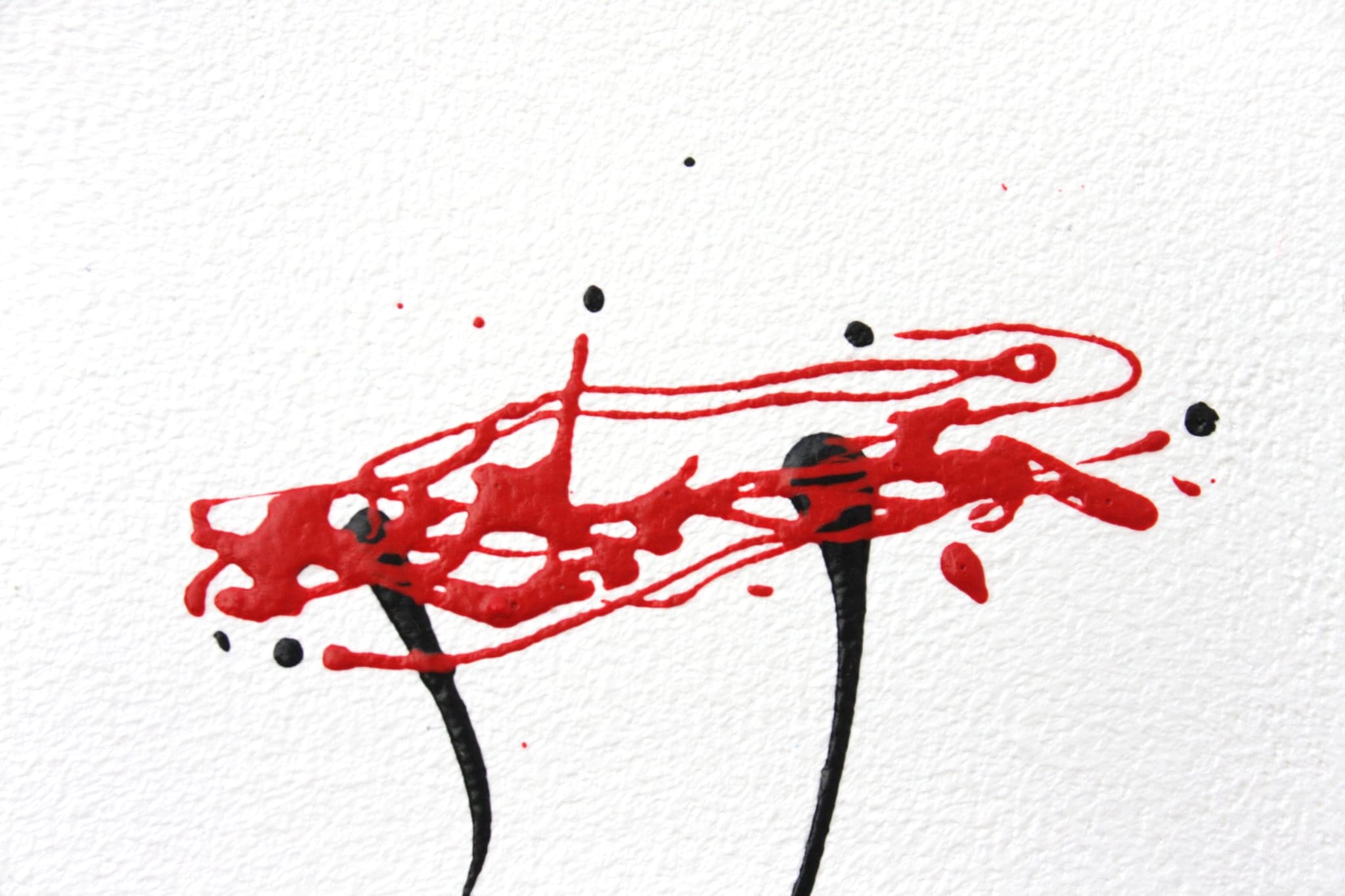 Close view of a red splash broken into droplets across white canvas above two black strokes